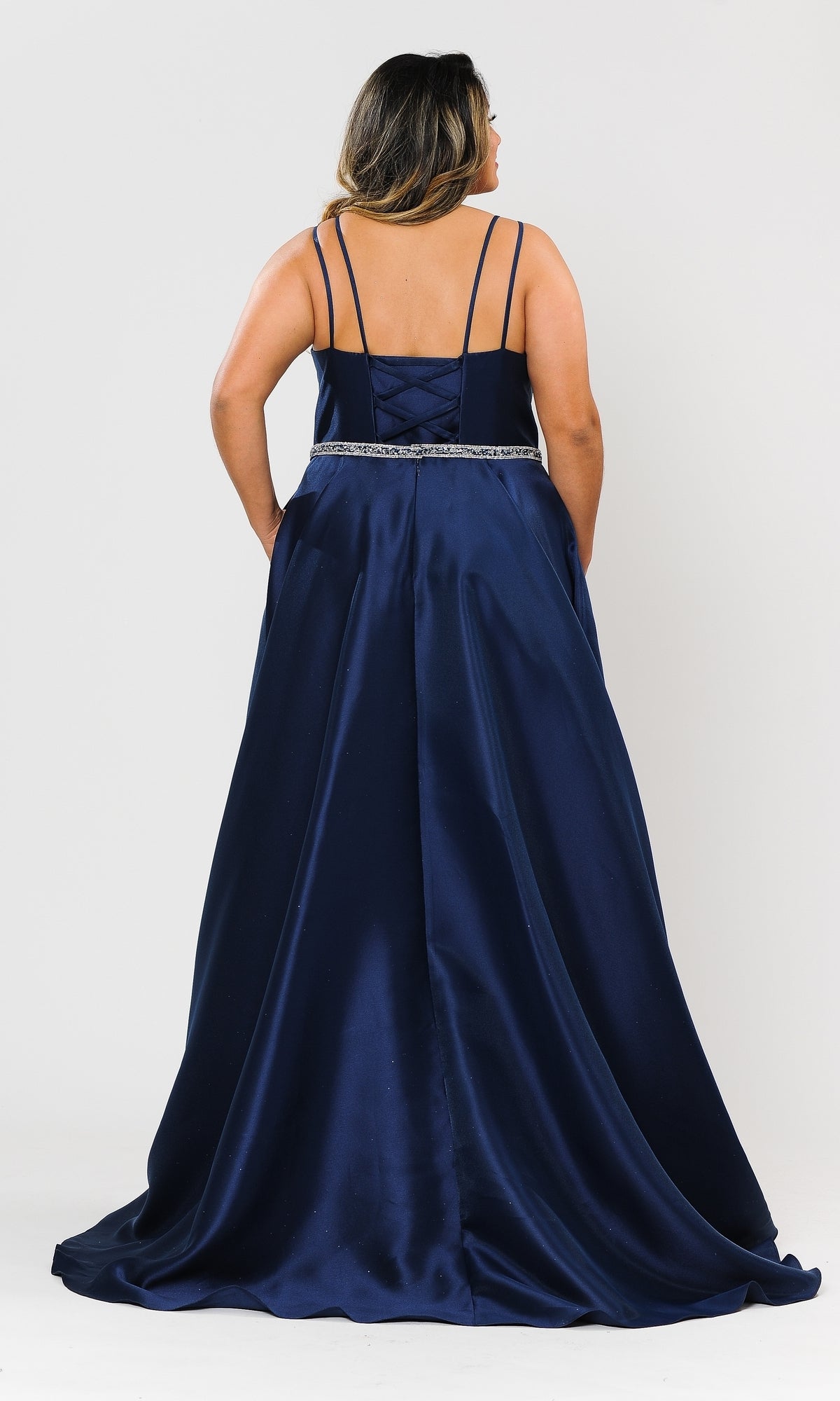 A woman faces away in the Plus-Size Long Prom Dress with Pockets W1106—an a-line, floor-length navy satin gown with thin straps, pockets, and a jeweled waistband.