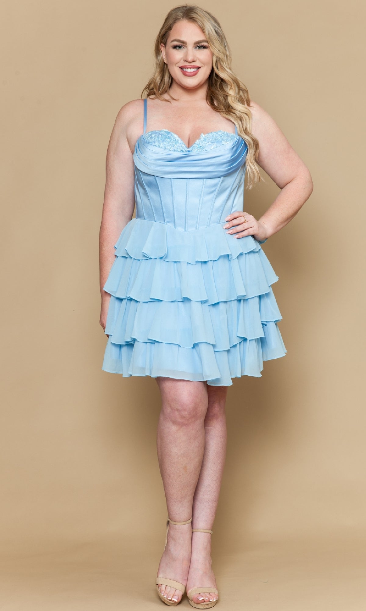 A woman poses against a beige background, smiling in nude heels and wearing the Poly USA W1196 Short Plus Size Homecoming Dress featuring a light blue chiffon A-line skirt and satin corset bodice.