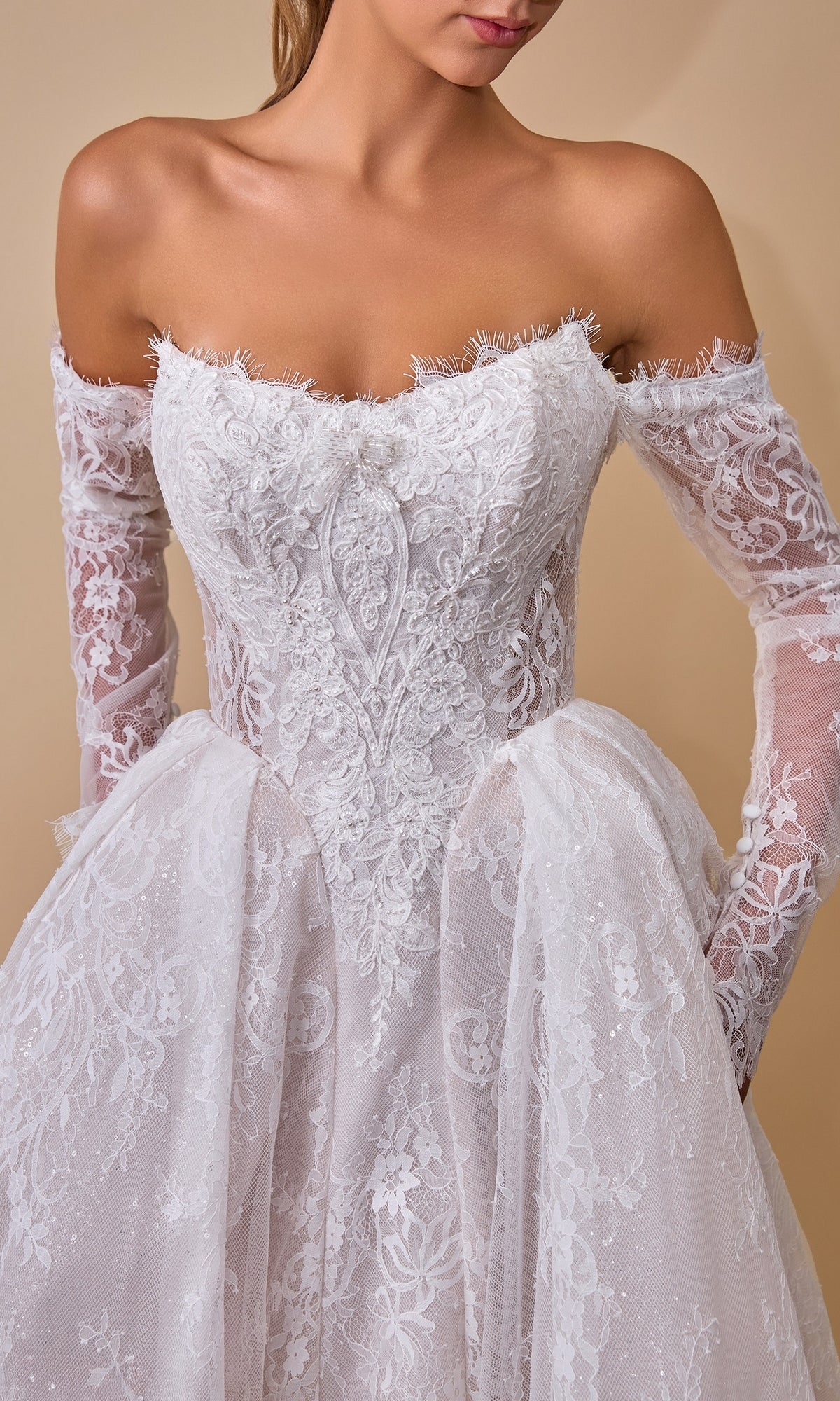A woman wearing the Andrea & Leo WL079 long wedding dress, an off-the-shoulder bridal gown featuring long lace sleeves and a fitted bodice. Crafted from exquisite white lace with intricate floral detailing, this elegant lace and tulle A-line wedding dress beautifully blends classic romance with modern sophistication.