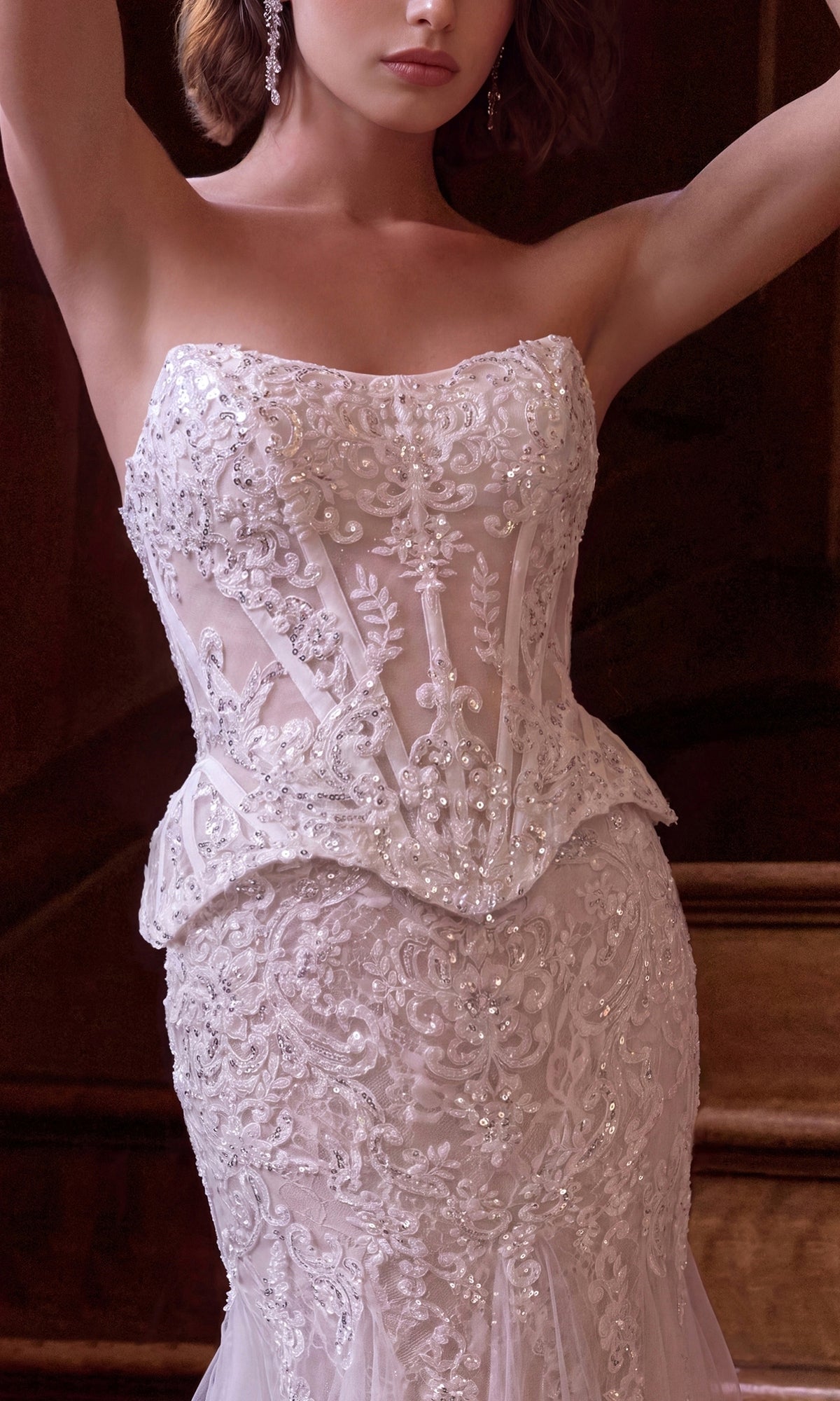 A woman stands indoors wearing the Long Wedding Dress: Andrea & Leo WL091—a strapless white gown featuring intricate beading, a fitted bodice adorned with floral embroidery, a flattering mermaid skirt, and delicate beaded lace corset detailing.