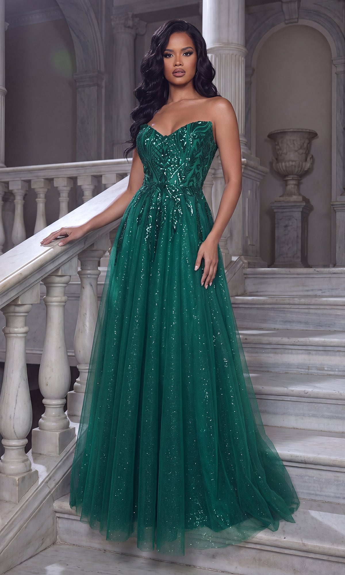 An elegant woman stands on a marble staircase in a classical interior, wearing the Portia and Scarlett XO134 long formal dress in emerald featuring a strapless design, sweetheart neckline, and sparkling embellishments.