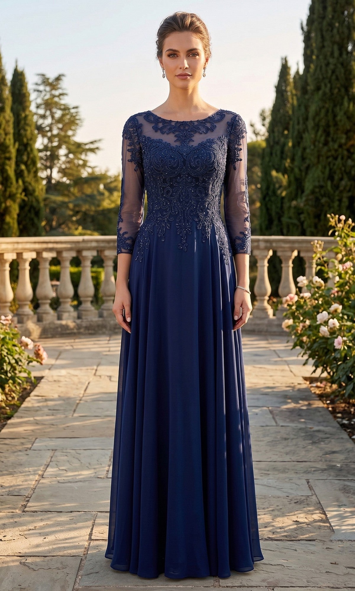A woman wearing the Long Prom Dress: Chicas XR6014 in navy, featuring an embellished bodice and sheer sleeves, stands on a stone walkway in a garden with trees and flowers.