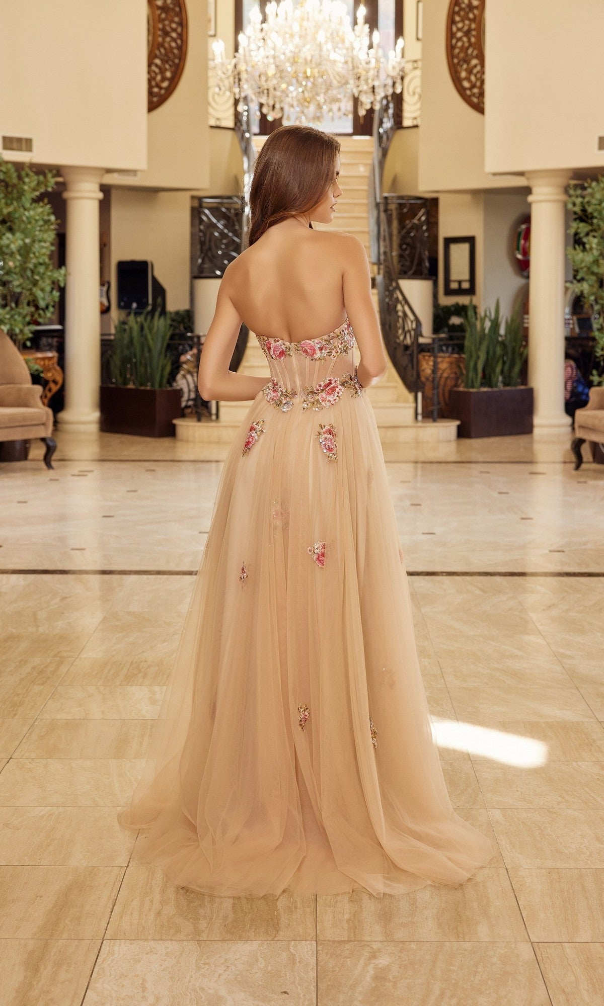 A woman stands in an elegant foyer wearing the floor-length, strapless Nox Anabel Y1803 prom dress, featuring delicate floral embroidery in a nude hue that radiates sophistication and charm.
