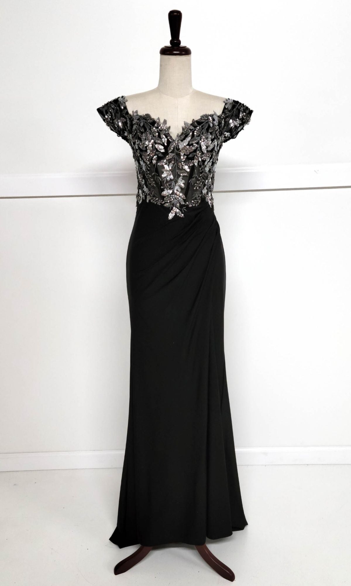 The Sequin-Bodice Long Prom Dress (Chicas YG5027) features a black sequin corset bodice, silver floral embroidered cap sleeves, and a floor-length skirt, displayed on a dress form.