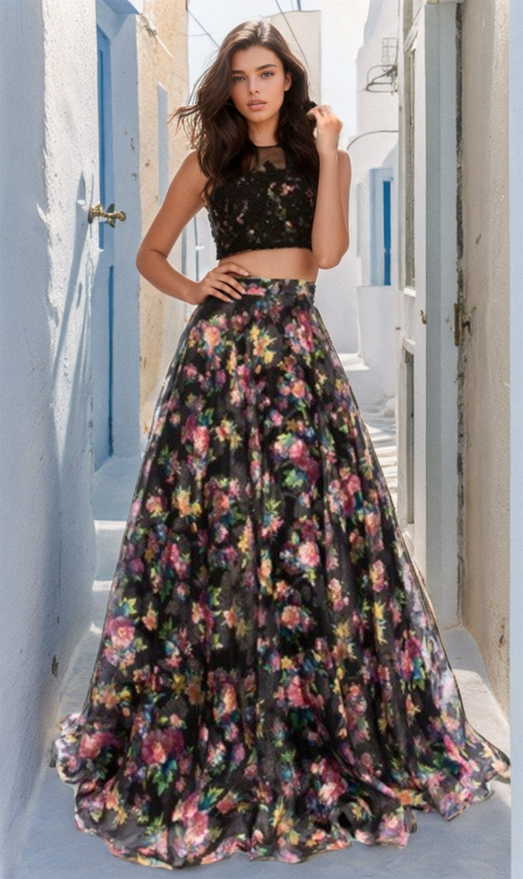 A woman stands in a sunlit alley wearing the Two-Piece Floral-Print Long Prom Dress B6803, featuring a black crop top and matching full-length skirt.