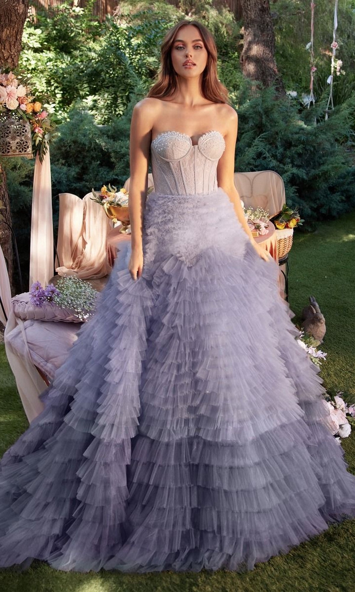 A woman stands outdoors in the Tiered Strapless Ombre Pink Prom Ball Gown A0767, featuring a structured bodice and full layered skirt. Flowers and greenery surround her, enhancing the romantic elegance of her look.