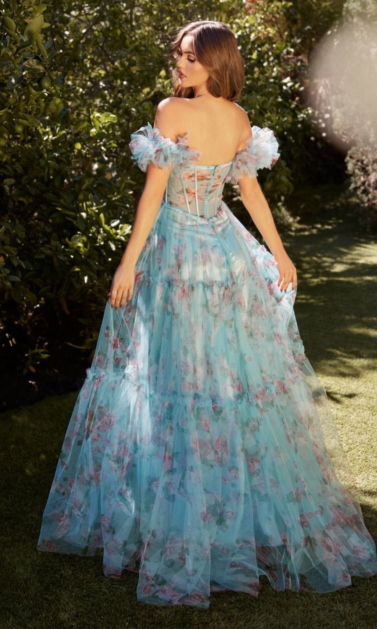 A woman stands outside in the Puff-Sleeve Long Blue Print Prom Dress A1285, featuring a corset-style bodice and off-the-shoulder puff sleeves, surrounded by lush greenery.