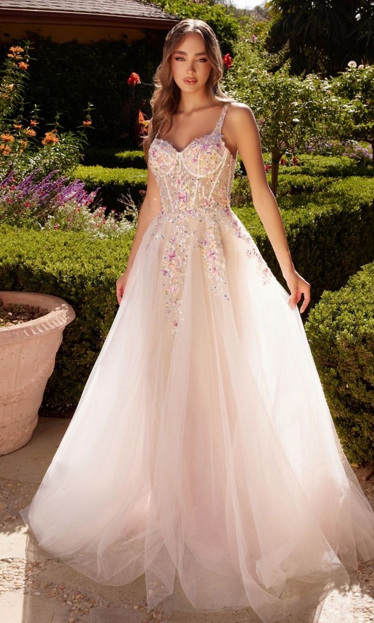 Outdoors in a garden, a woman wears the Floral-Bodice Off White Long Prom Ball Gown A1288, featuring floral embellishments and a sheer tulle skirt for an elegant, romantic look.