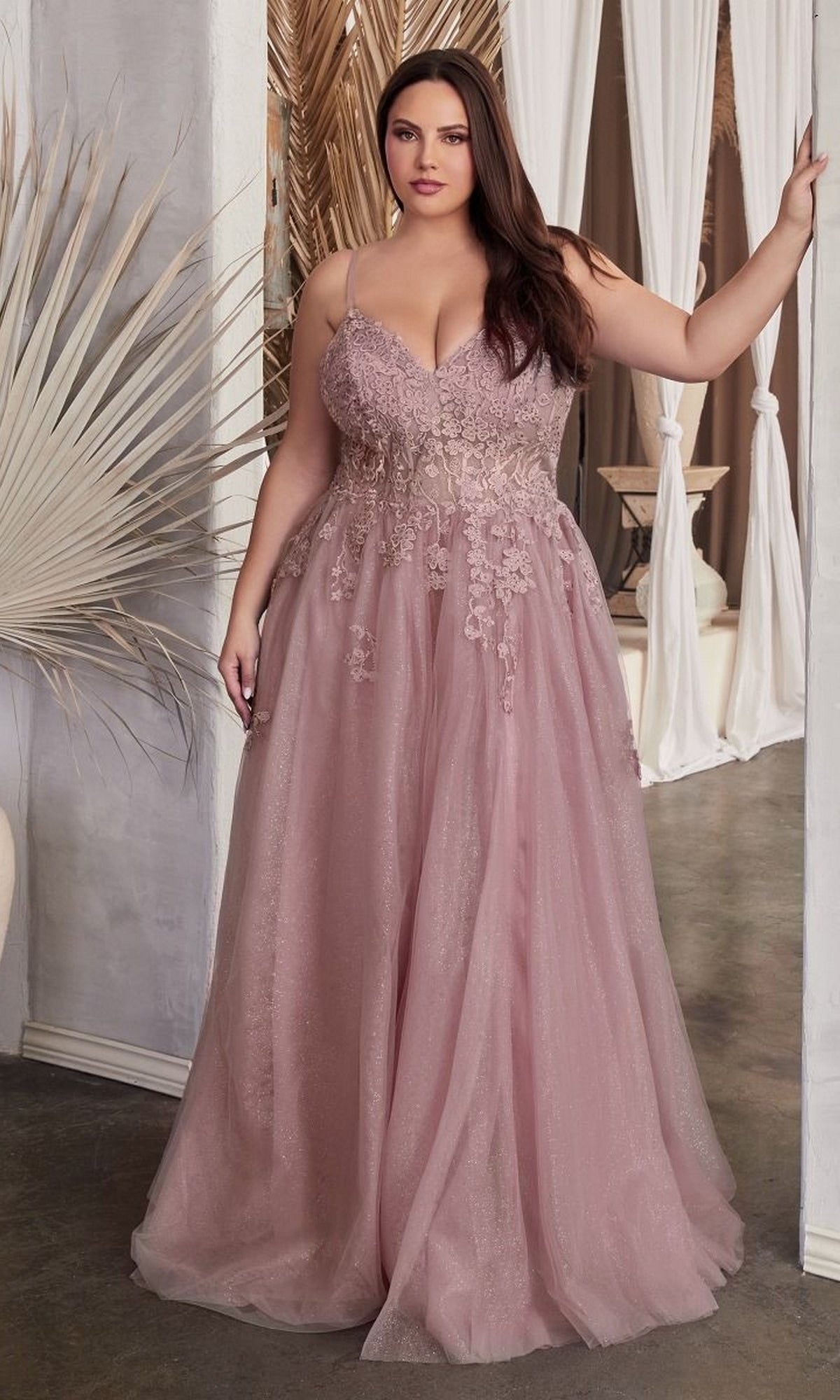 A woman in a blush pink Lace-Up Back Plus-Size Long Prom Ball Gown C148C with lace and floral details stands indoors, holding a doorway.