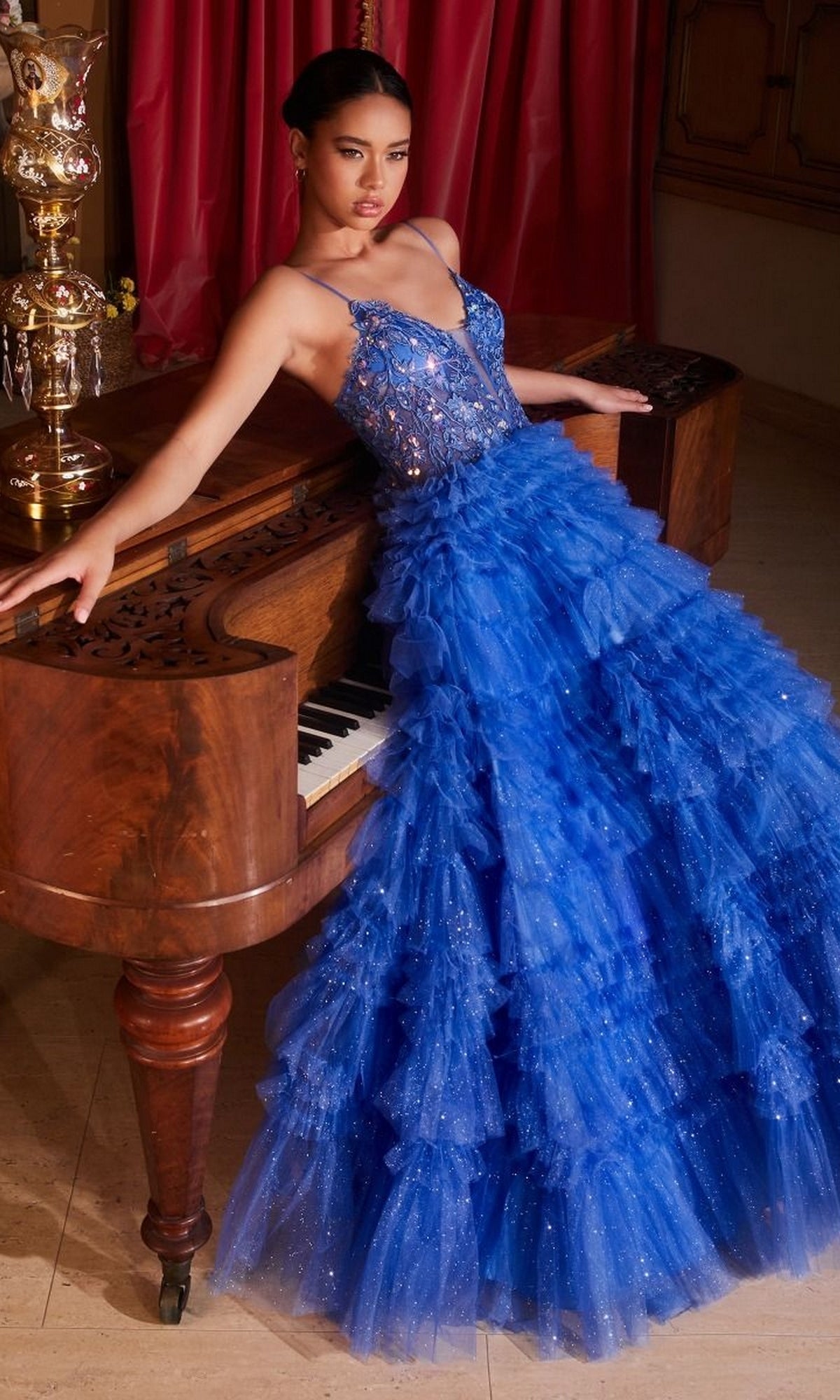 A woman in the Sheer-Corset Long Glitter-Tulle Prom Ball Gown C152 poses leaning against a wooden grand piano in an elegantly decorated room.