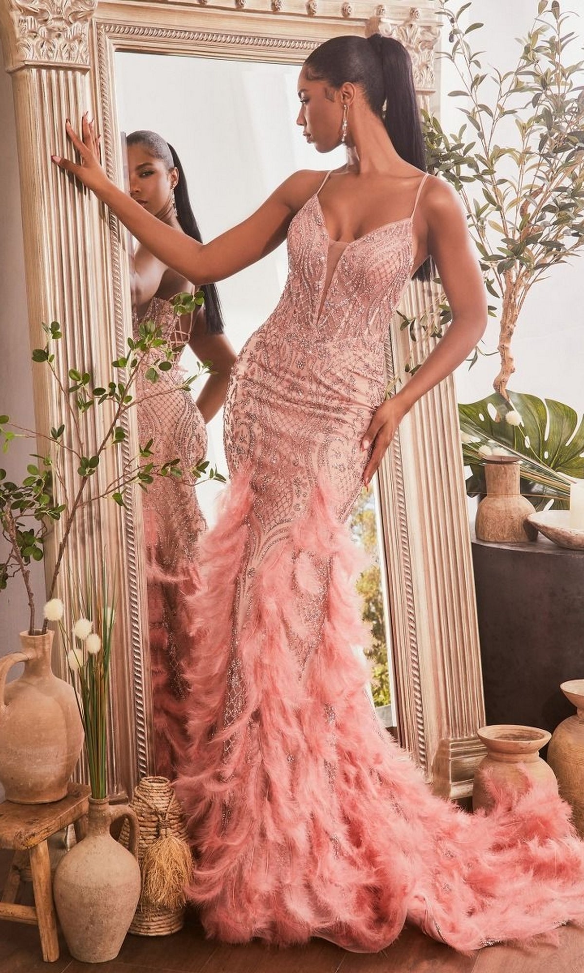 A woman in the Feather-Trimmed Glitter-Print Long Prom Dress CC1608 stands before a large ornate mirror, surrounded by decorative vases and green plants.