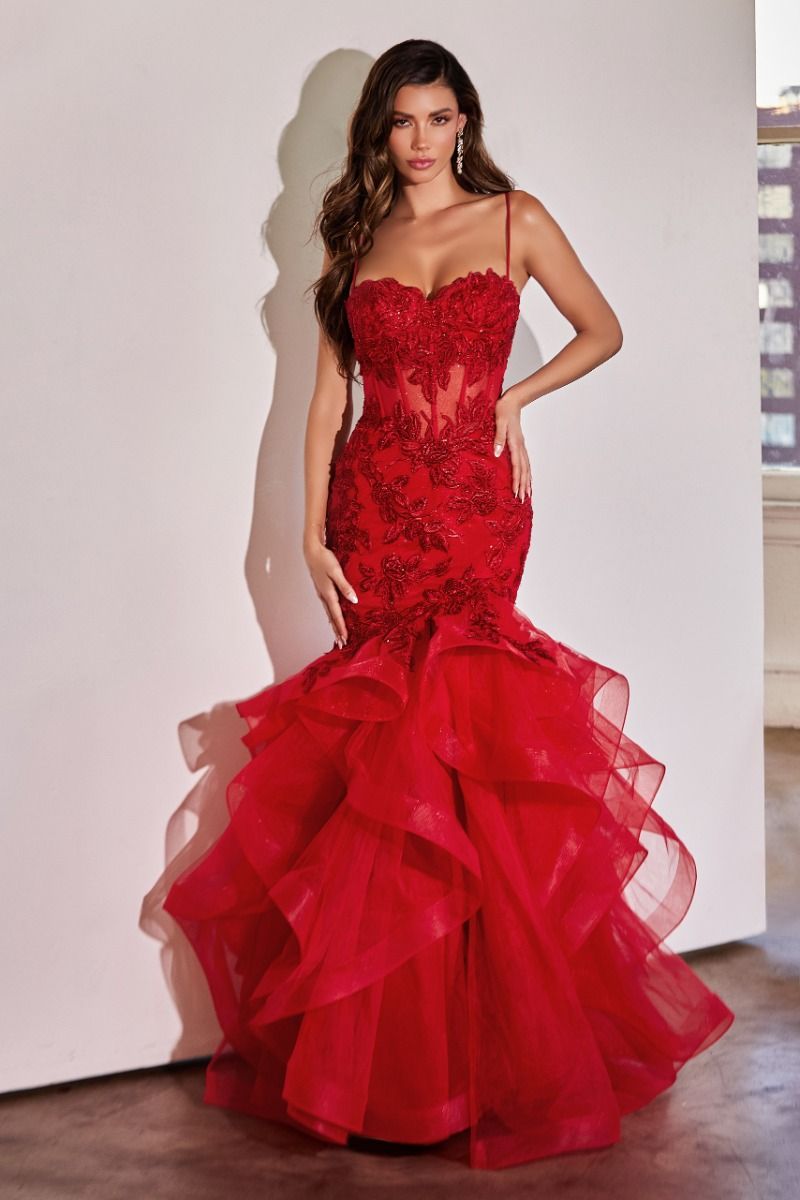 Indoors, a woman wears the Ladivine CC8915 Long Ruffle Mermaid Prom Dress, featuring a fitted red silhouette with lace detailing, sheer panels, and layered ruffles at the skirt.