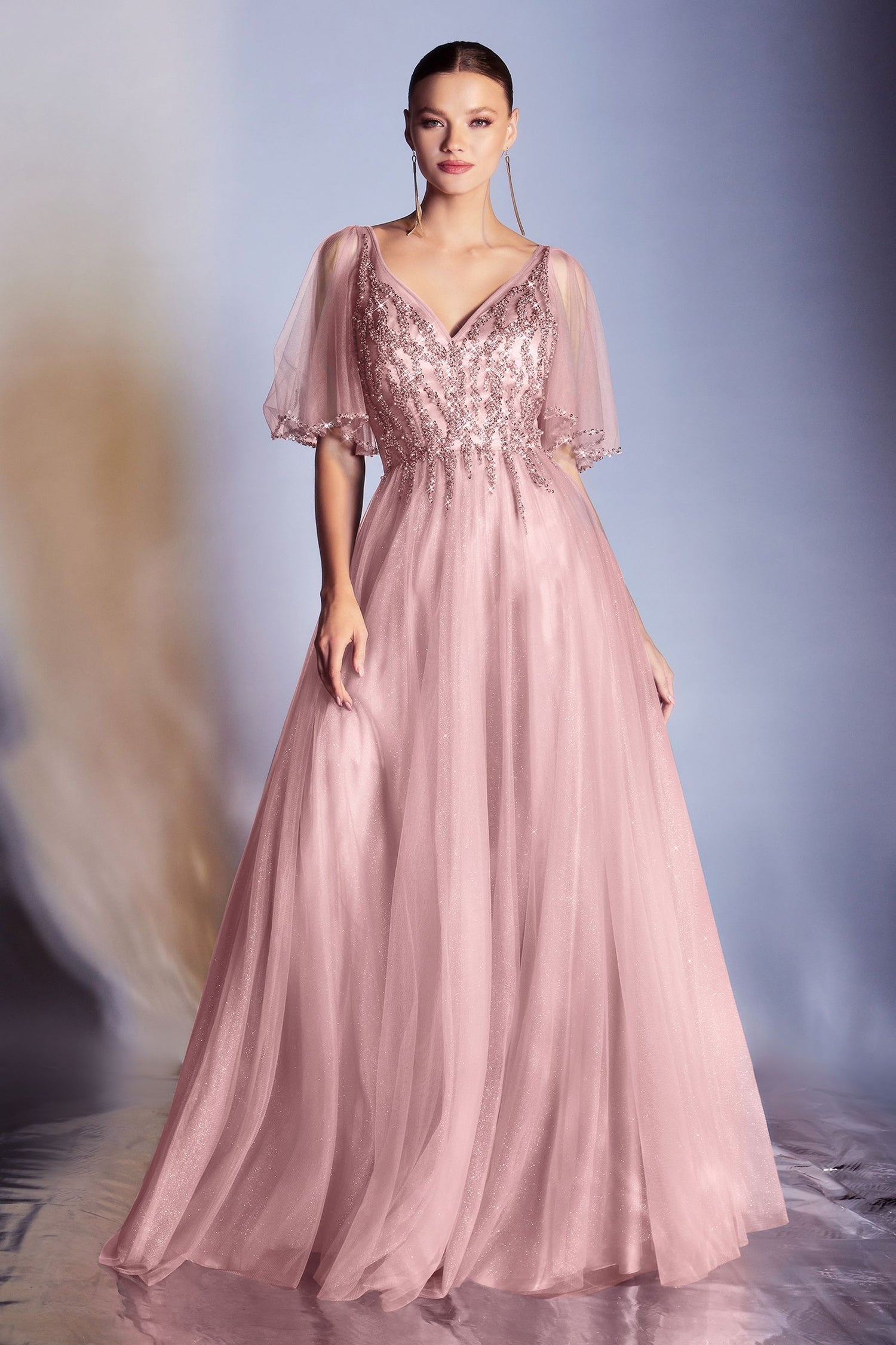 A woman models the Ladivine CD0175 Bell-Sleeve Glitter Formal Dress in blush pink, featuring sheer bell sleeves and sequin-embellished bodice, posed against a soft gradient background.