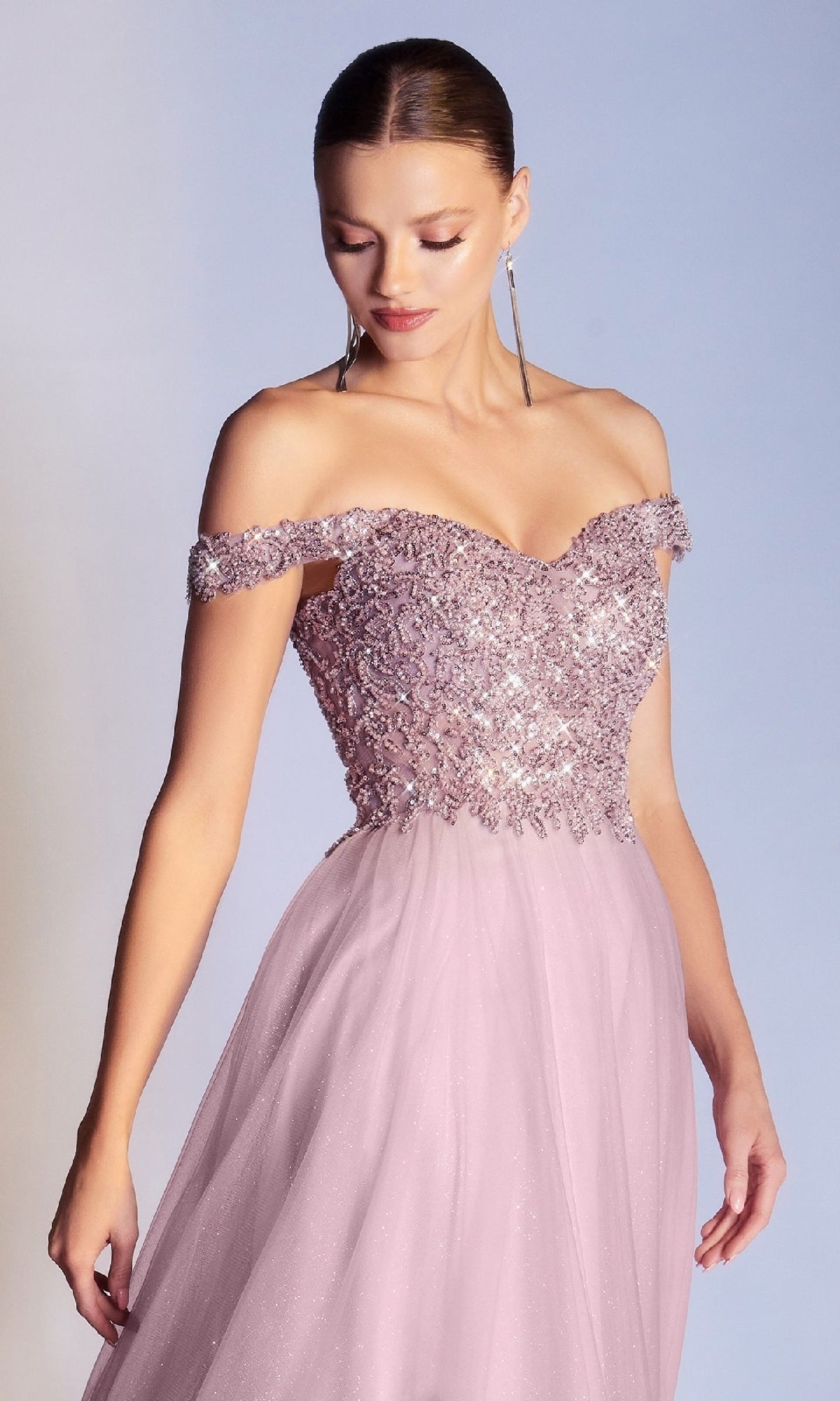 A woman wears the Ladivine CD0177 Beaded-Bodice Long Prom Dress—a floor-length, light pink gown with a sparkling bodice and sheer flowing skirt—standing against a plain background.