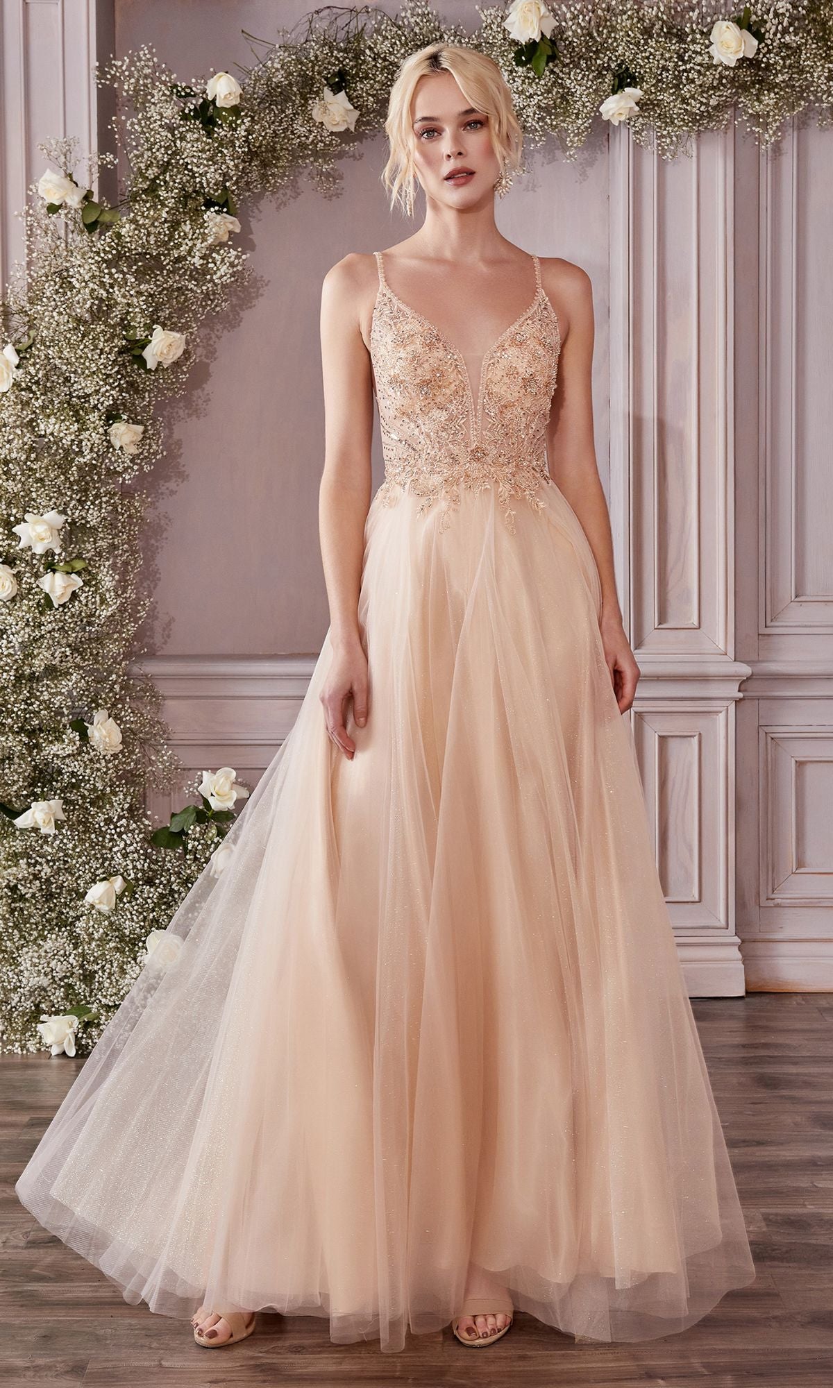 A woman stands indoors before a floral arch and wood paneling, her Embellished-Bodice Long Tulle Prom Dress CD0195 in pale peach catching the light.