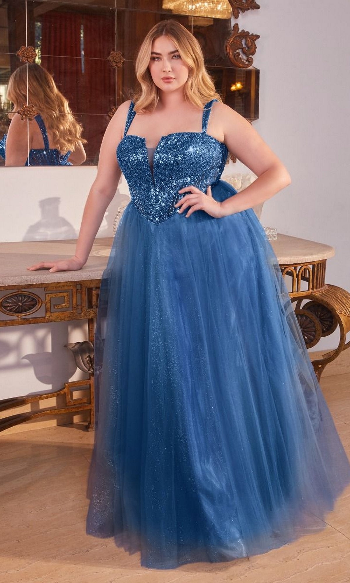 A woman stands by a table wearing the Plus-Size Sequin-Bodice Long Prom Dress CD0217C—a blue, floor-length gown with sparkling bodice and tulle skirt, perfect as an affordable formal dress for any special occasion.