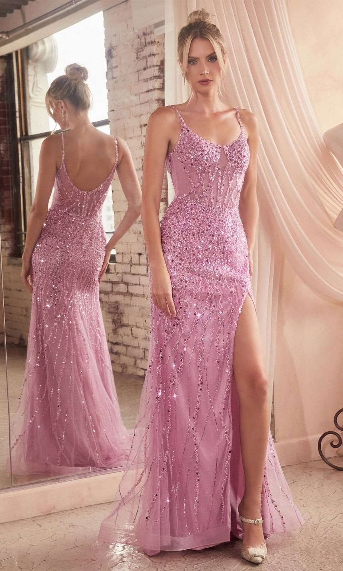 A woman wearing the Sheer-Bodice Long Beaded Prom Dress CD0220 in light pink, featuring a thigh-high slit, stands by a mirror to highlight both the front and back views of the gown.