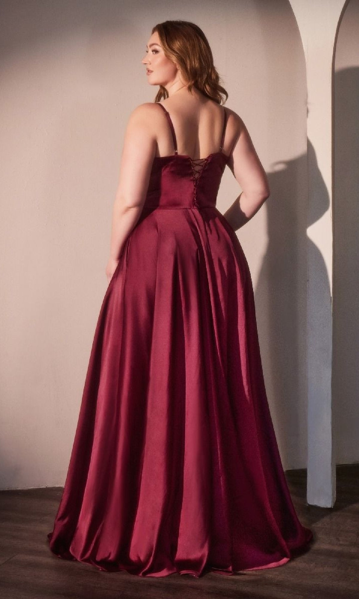 A woman in a sleeveless, floor-length Ladivine CD337C Plus-Size Long A-Line Prom Dress stands with her back to the camera in a softly lit room.