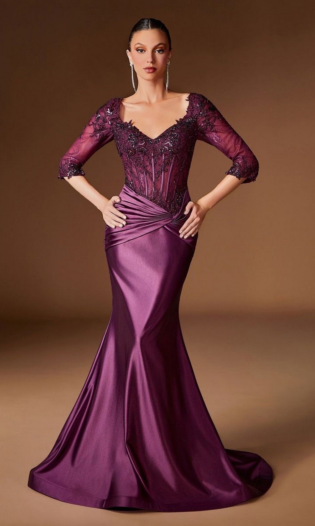 A woman poses with hands on hips in the Lace-Bodice Long Gold Prom Dress: Ladivine CD731, featuring a fitted, floor-length silhouette and lace bodice, set against a plain brown background.