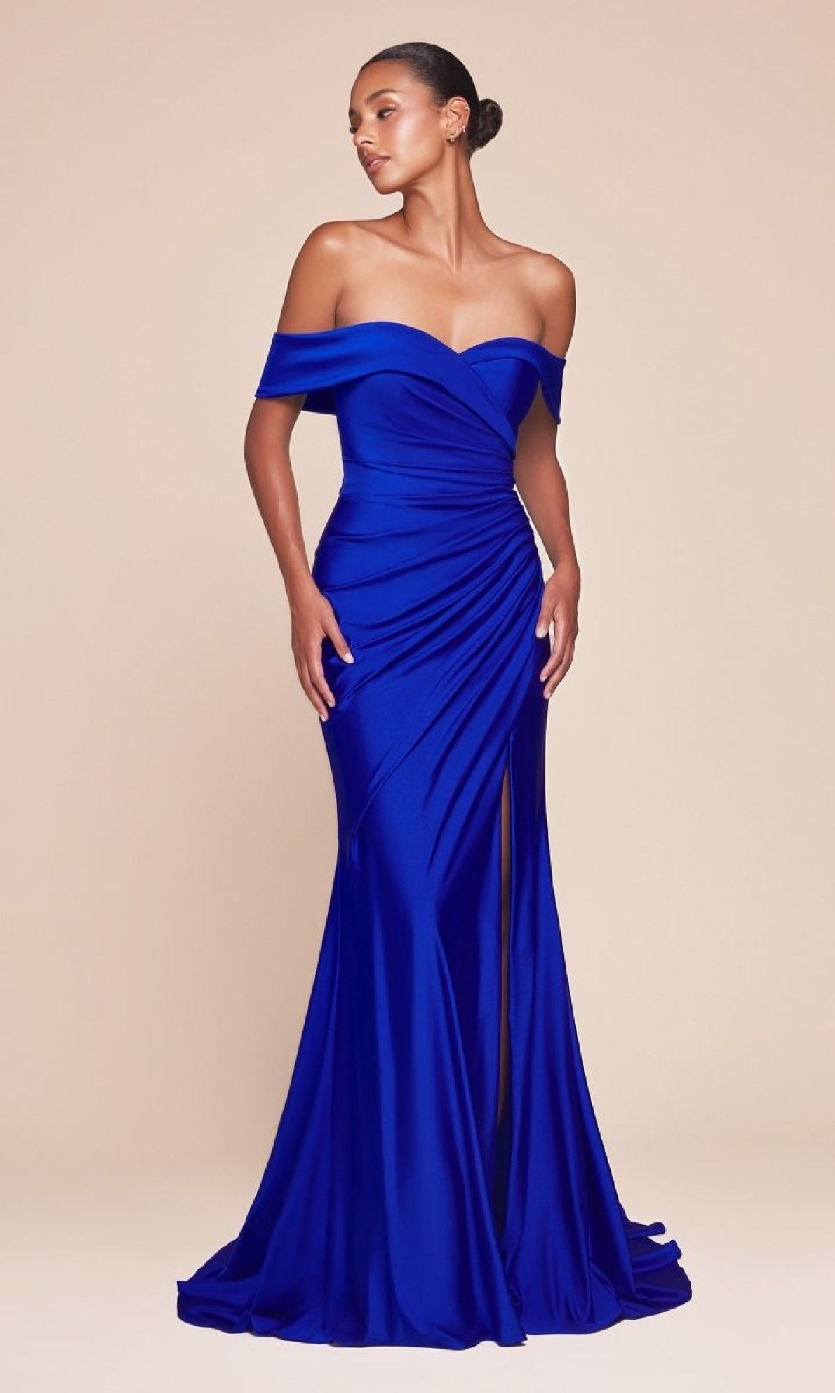 A woman stands against a beige background wearing the Off-the-Shoulder Long Prom Dress: Ladivine CD790 in royal blue, featuring a floor-length satin design with a thigh-high slit and ruched detailing.