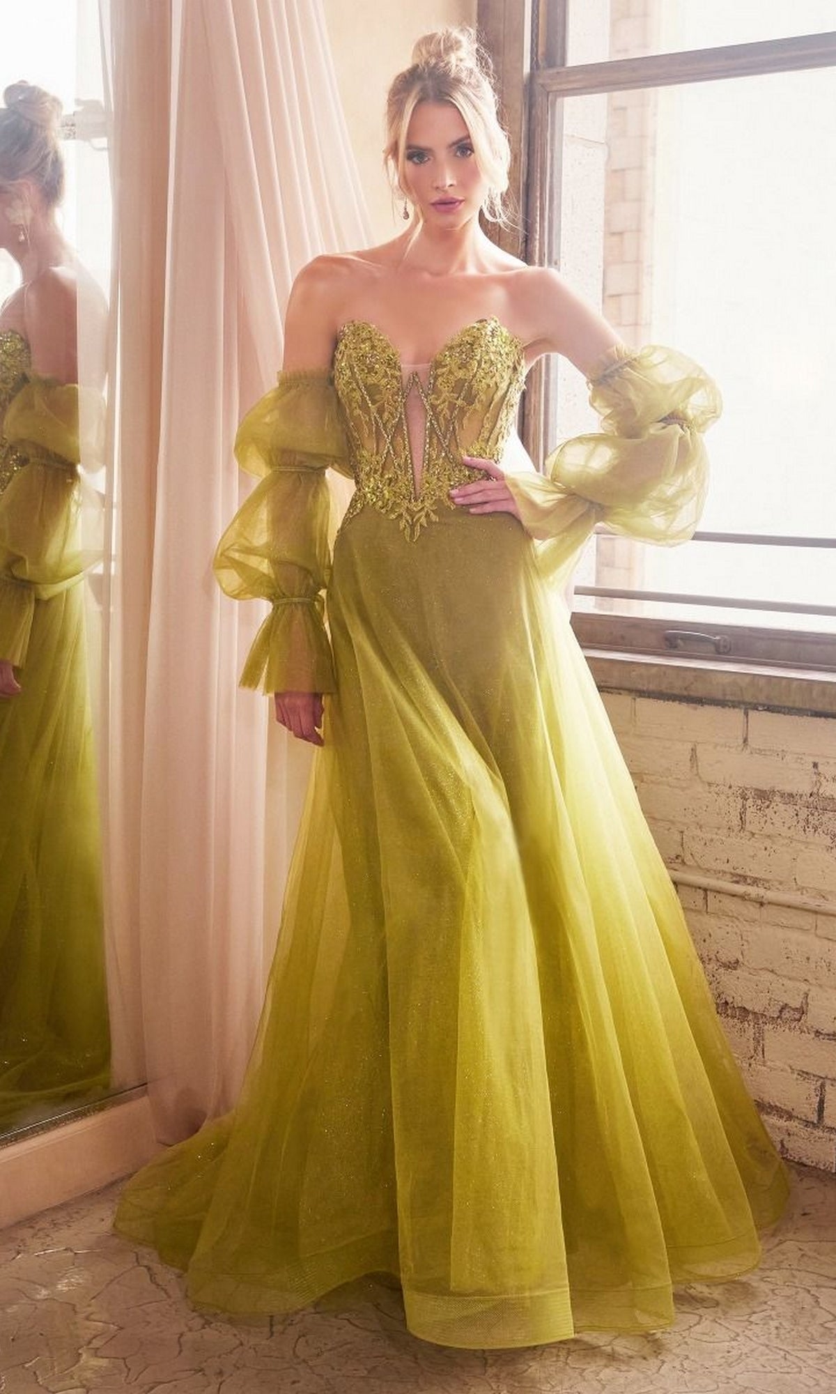 A woman stands indoors wearing the Long Sleeve Strapless Long A-Line Prom Dress CD830 in olive green tulle, featuring sheer puffed sleeves and delicate floral embroidery on the bodice.