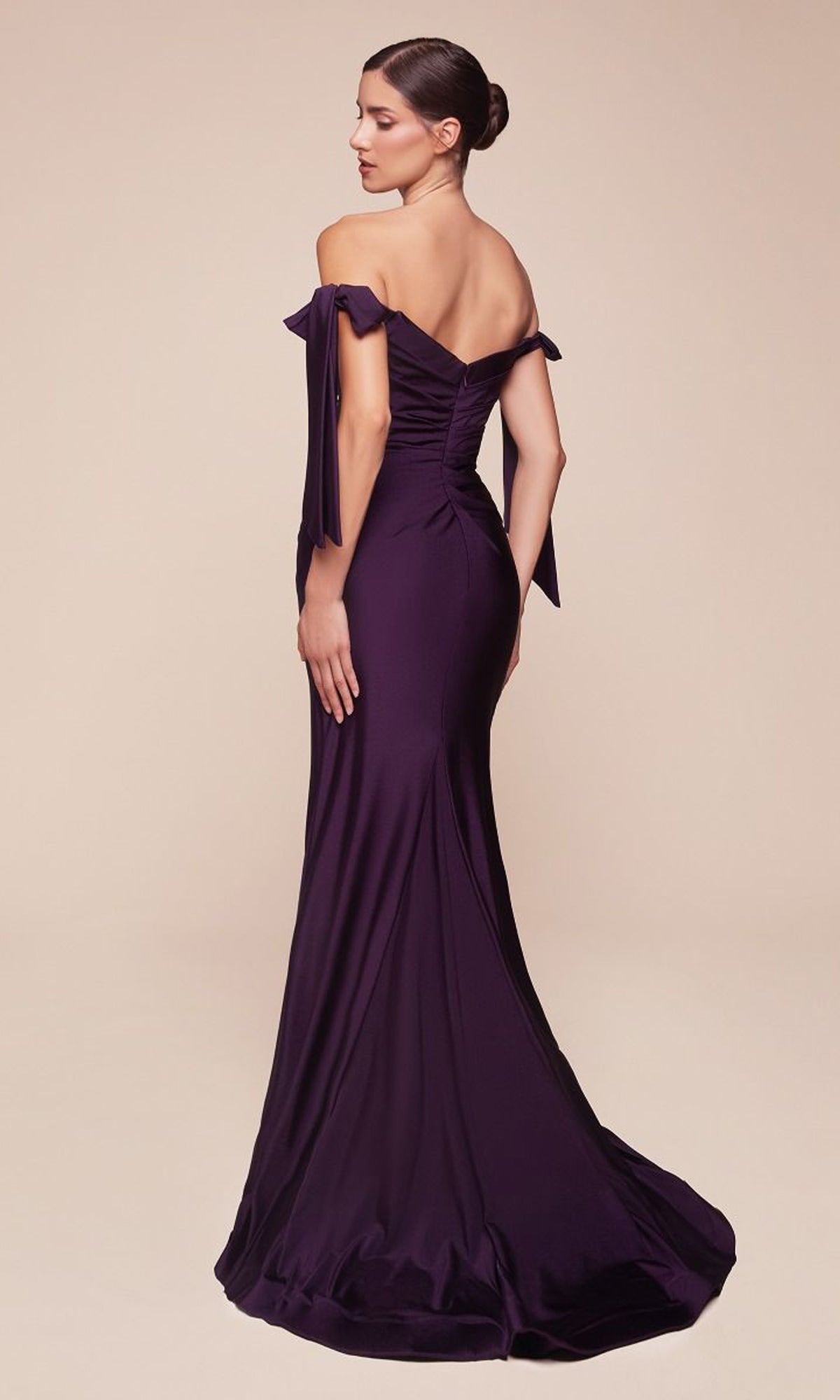 A woman in the Off-Shoulder Ruched Prom Dress: Ladivine CD943 stands with her back partially turned, highlighting the dress's fitted bodice and flowing stretch jersey floor-length design.