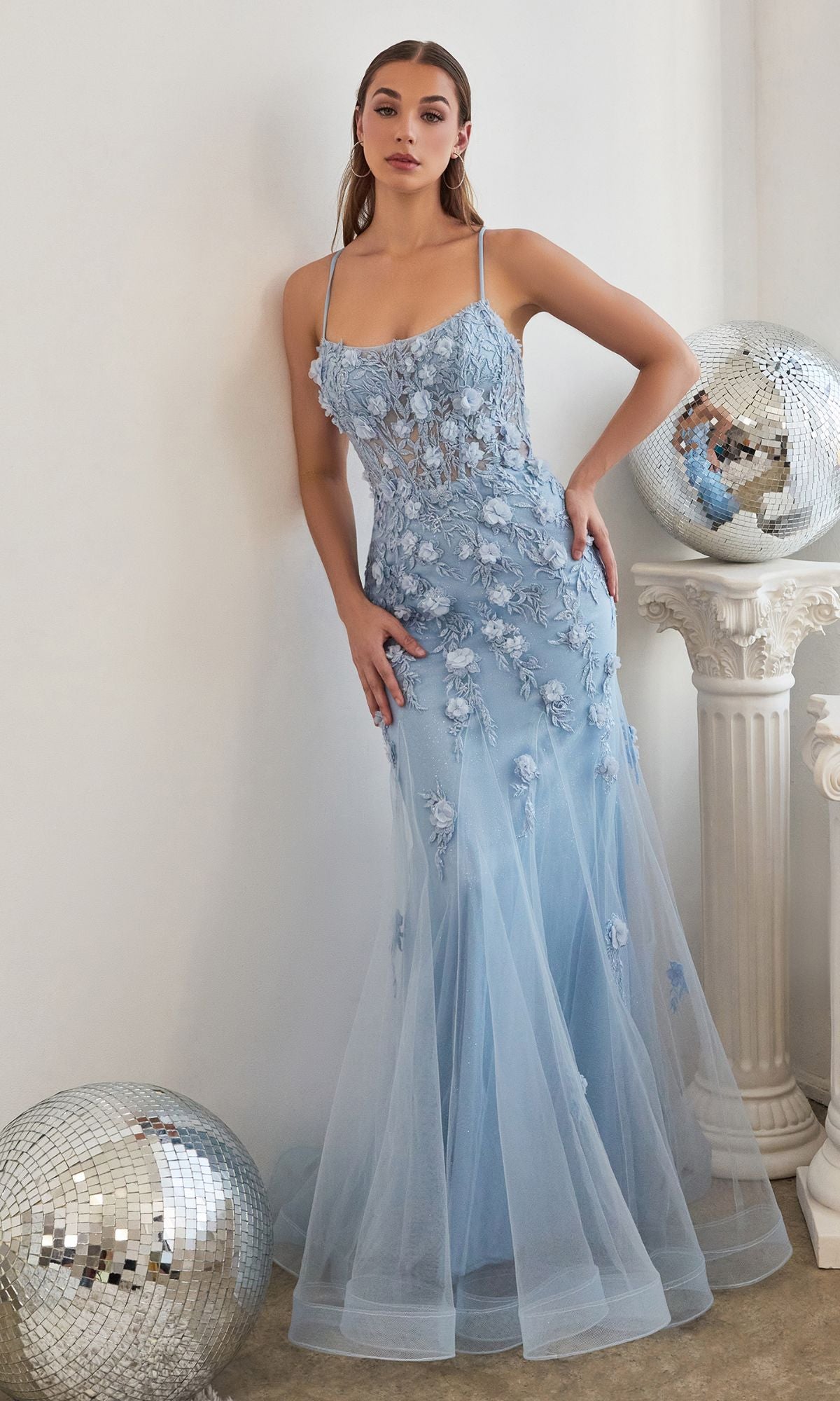 A woman in the Floral-Applique Long Mermaid Prom Dress CD995 stands against a white wall, with two disco balls and a white pedestal nearby.