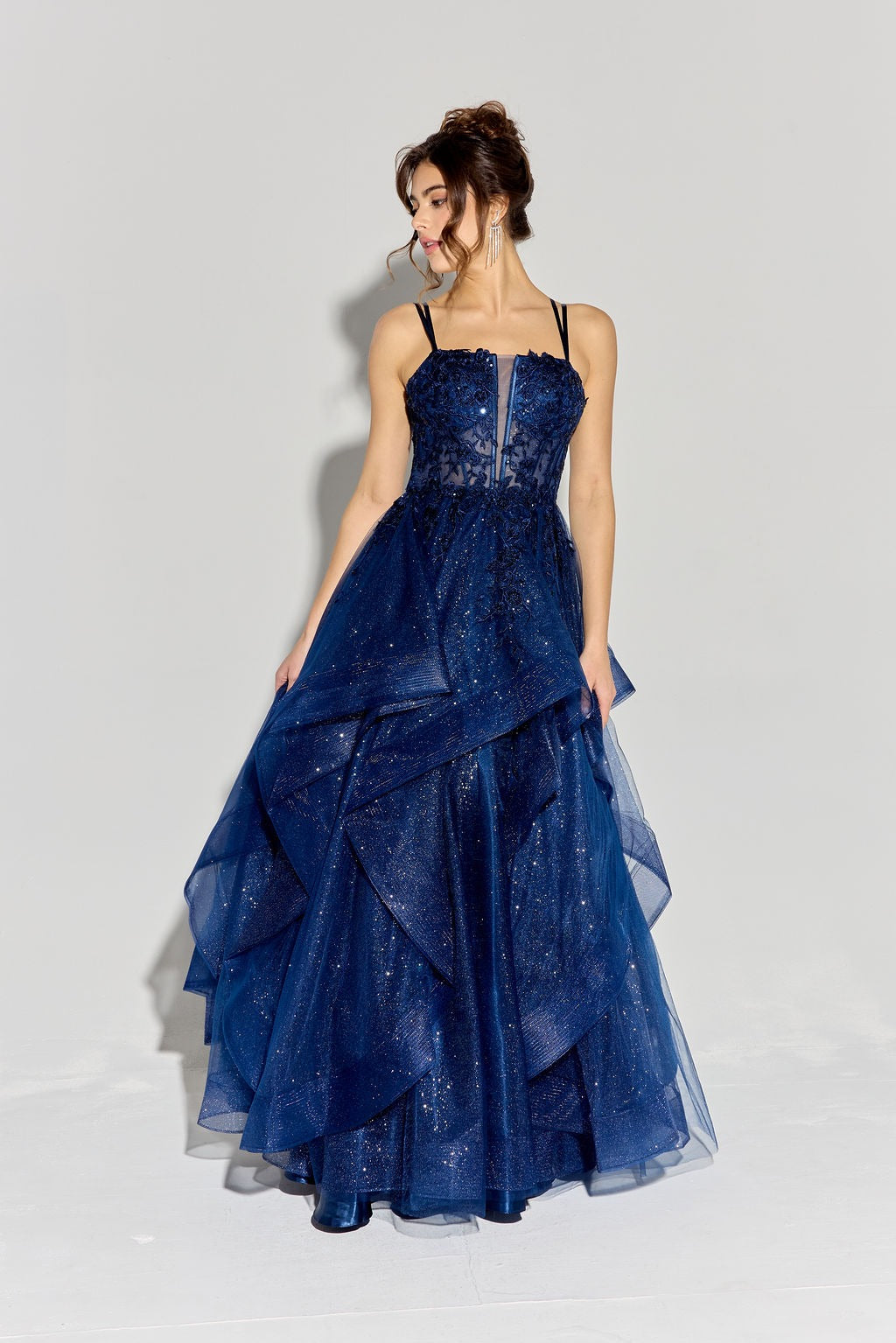 A woman models the Eureka EK157, a dark blue sparkly long prom dress with a glitter tulle skirt and thin black straps, standing against a plain light background.