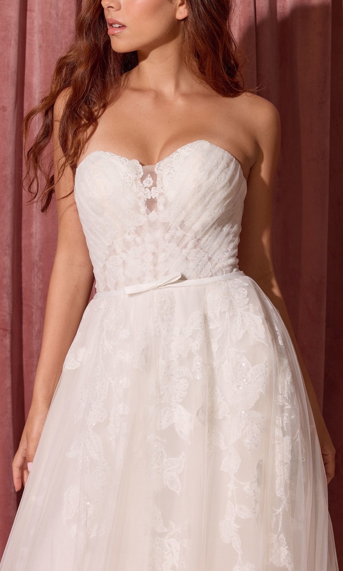 Woman wearing the Long Wedding Dress: Eureka EK165 with a fitted lace bodice and full tulle skirt, standing in front of a pink curtain.
