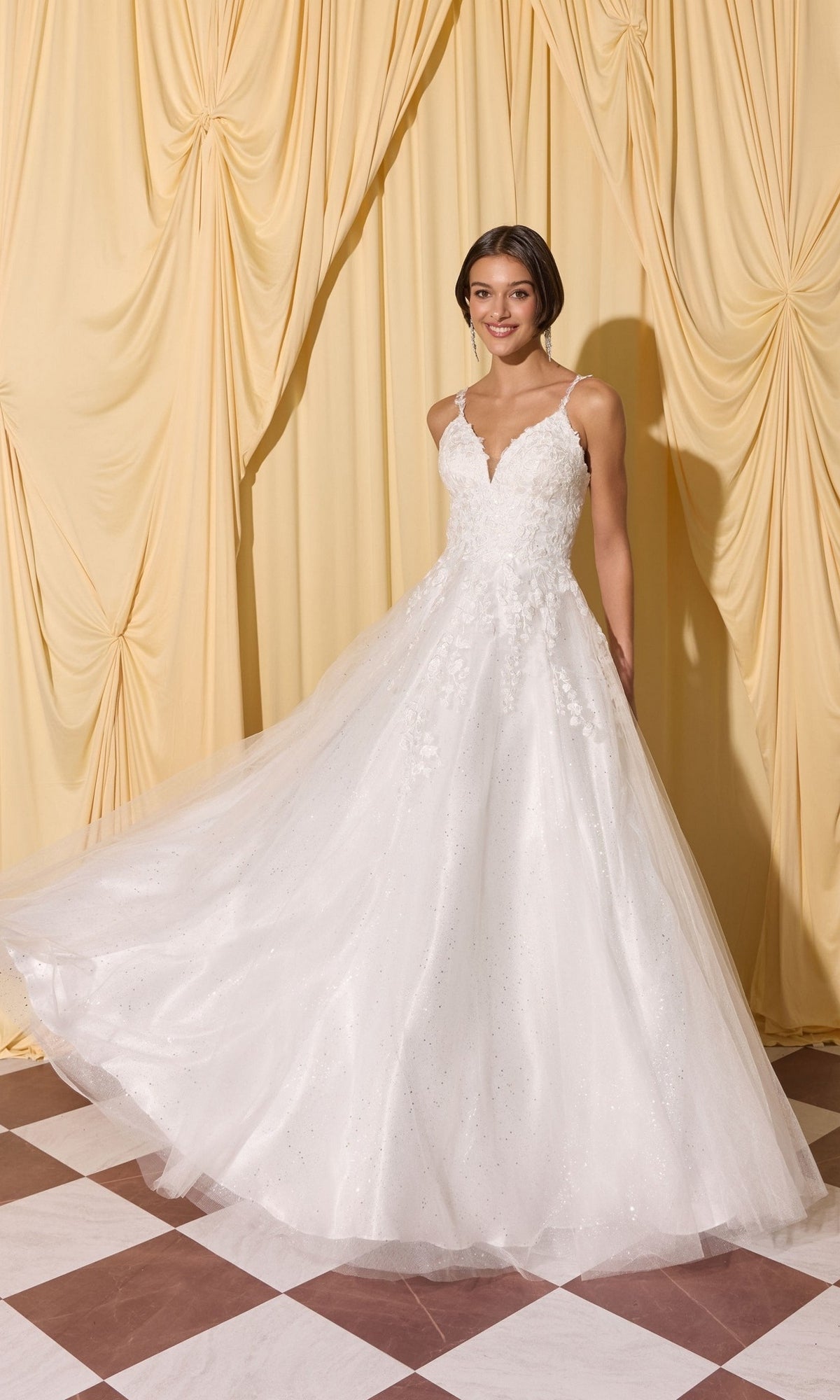 Woman in a Long Prom Dress: Eureka EK210, white, sleeveless, A-line with lace and 3D floral appliques stands on a checkered floor before cream draped curtains.
