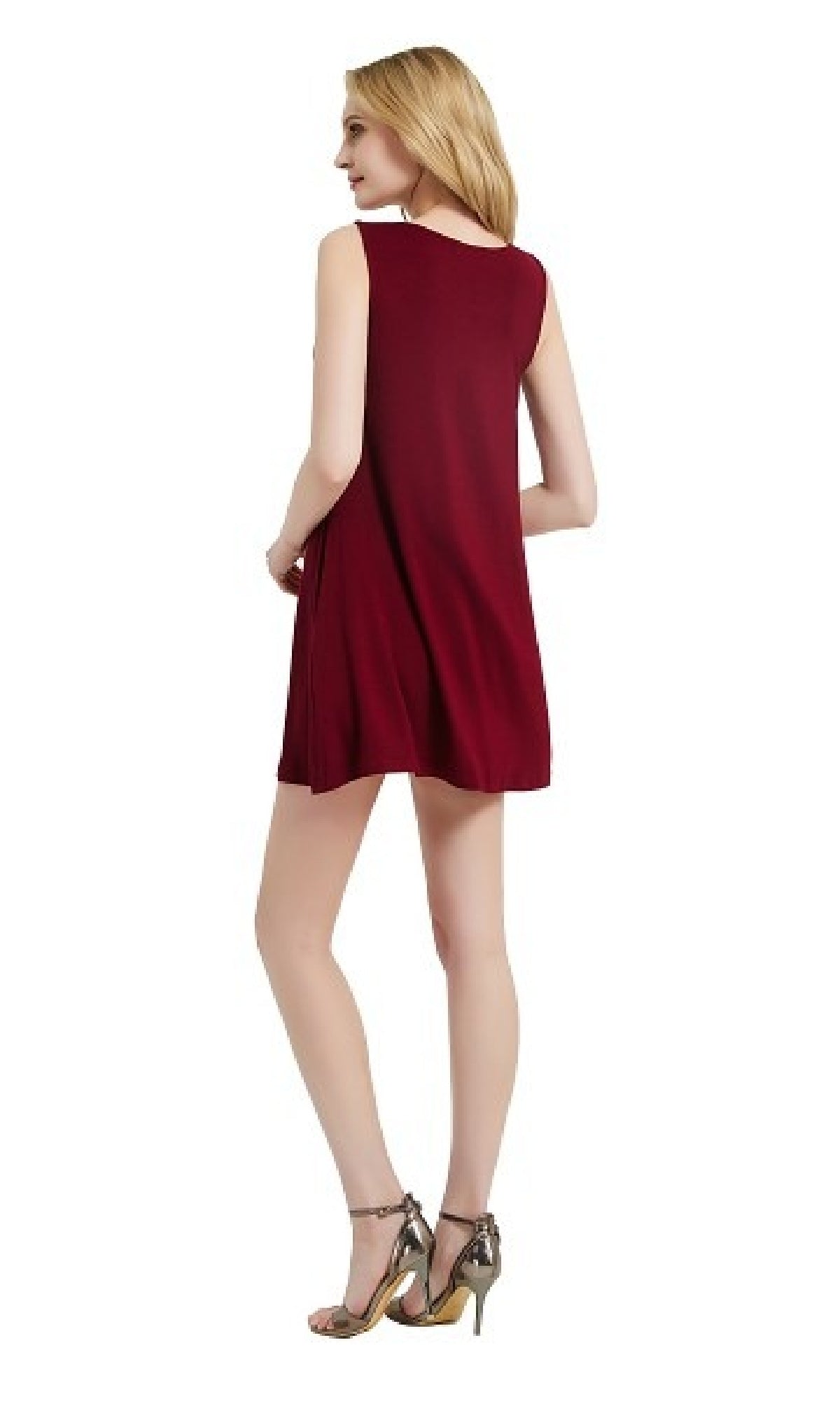 A woman stands facing away, wearing a sleeveless casual short t-shirt dress with pockets in burgundy and metallic high-heeled sandals against a white background.