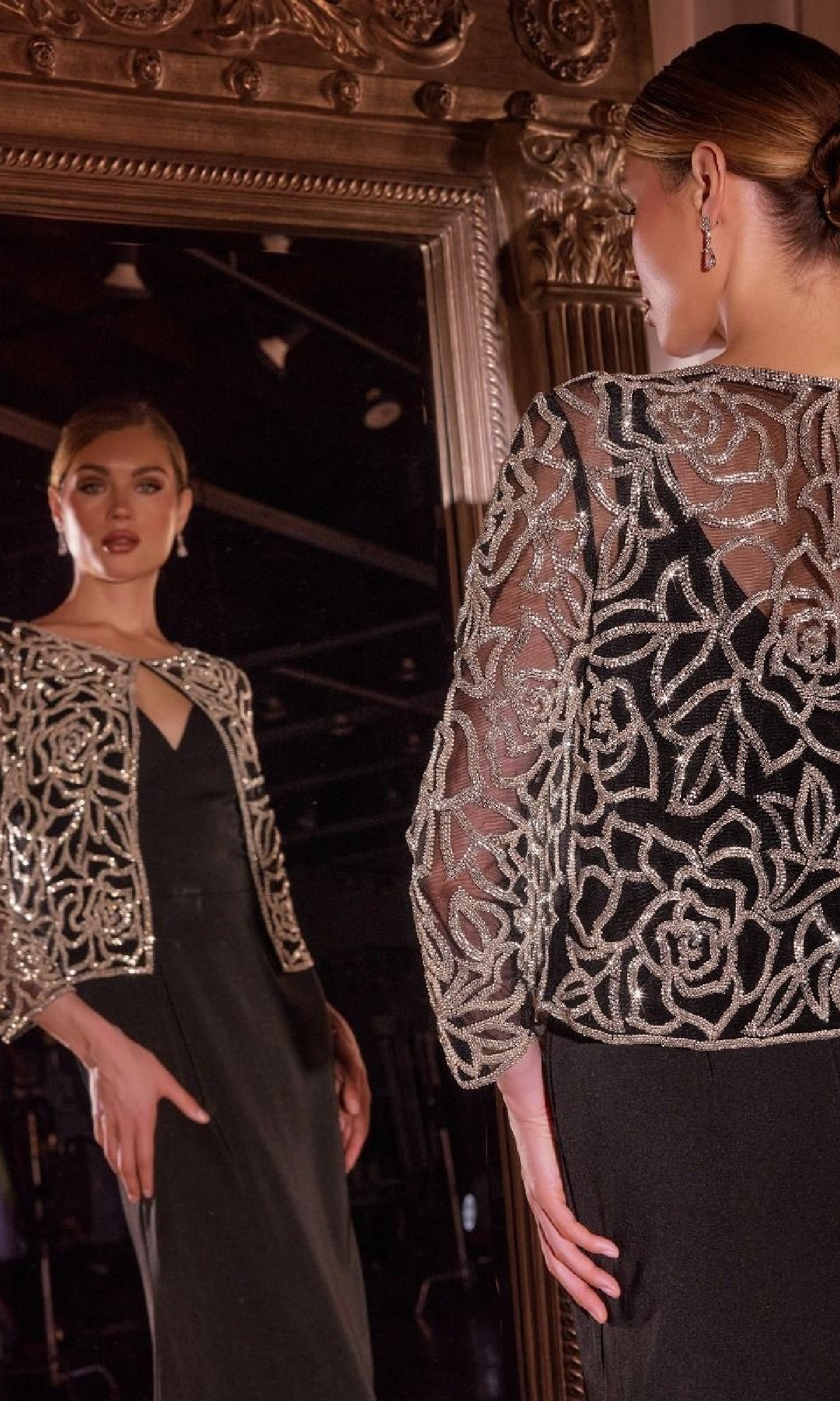 Wearing the Beaded-Jacket Long Formal Dress: Ladivine J881, a woman stands before a large mirror, her reflection displaying the gown’s ornate beaded jacket and elegant silhouette.