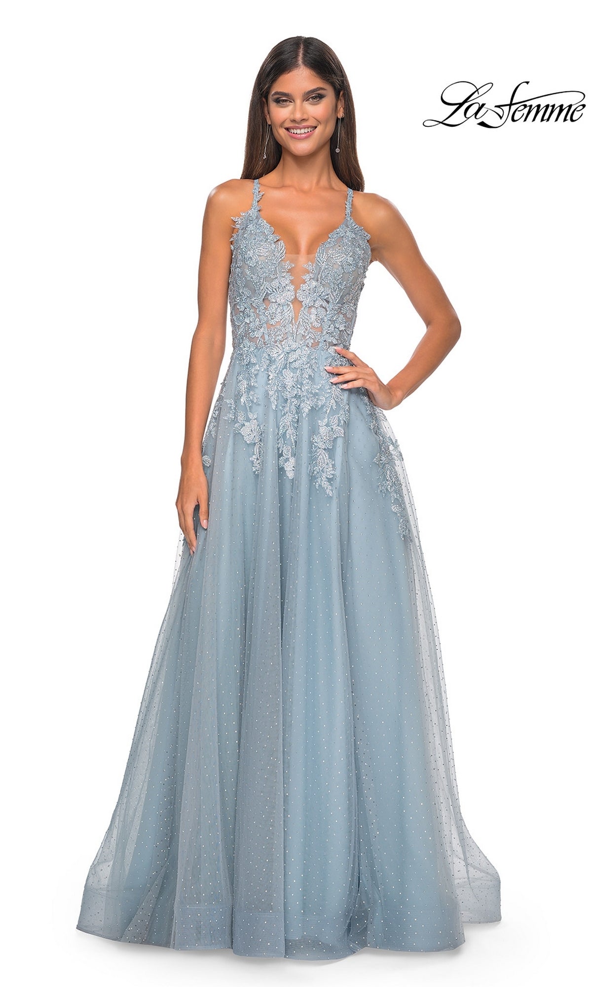 A woman wearing the La Femme Lace-Embroidered Long Prom Dress 32147 in light blue, featuring thin straps, a sheer bodice detail, floral lace appliqué, and a flowing tulle skirt.