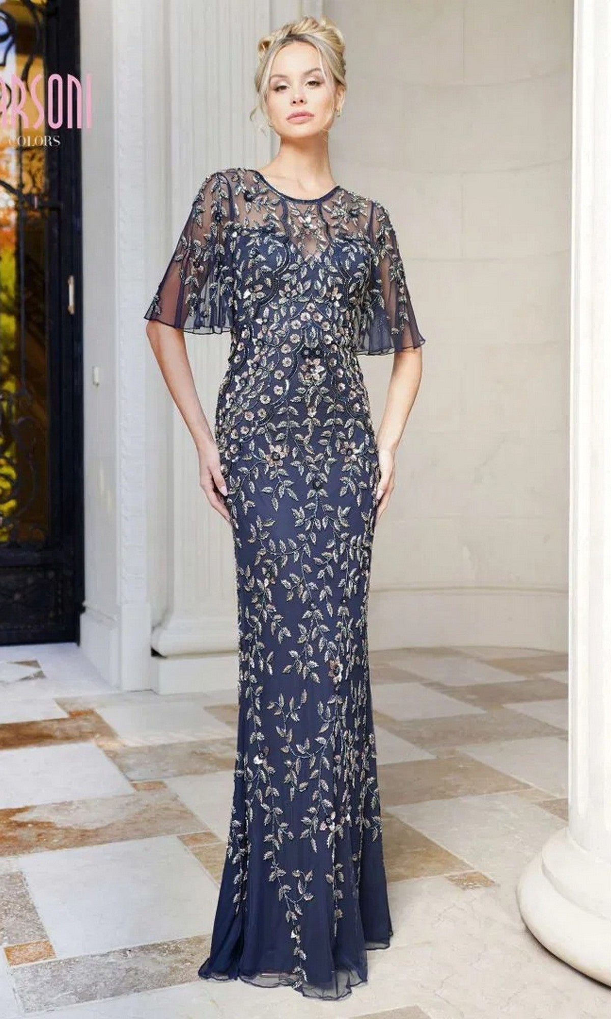 A woman stands indoors wearing the Marsoni MV1208, a long formal dress in Navy/Rosegold with gold floral embroidery, sheer short sleeves, and subtle sequin accents.