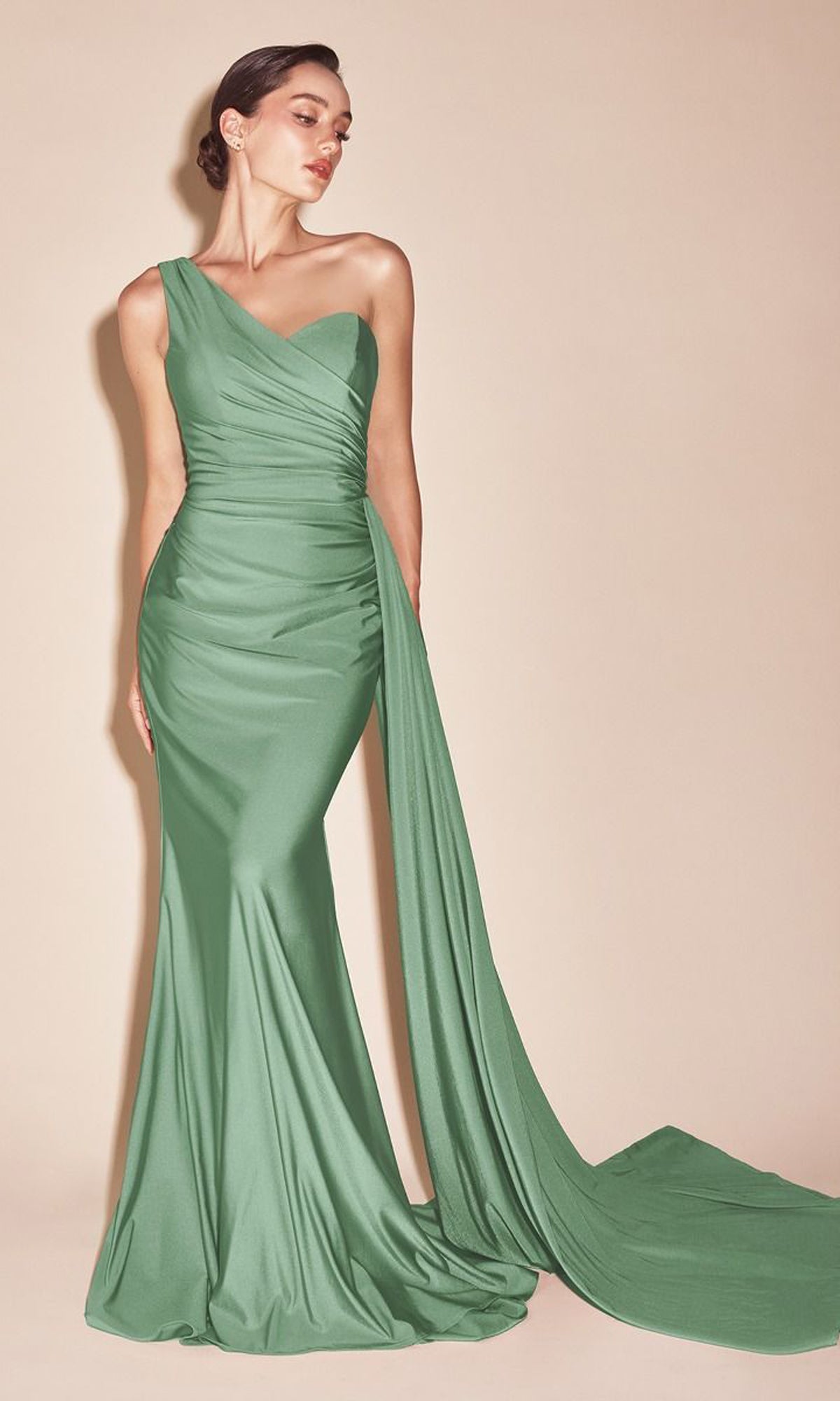 A woman stands against a beige background wearing the Plus-Size Long Sweetheart Prom Dress PT004C, a fitted sage green evening gown with one shoulder and a long, draped train.