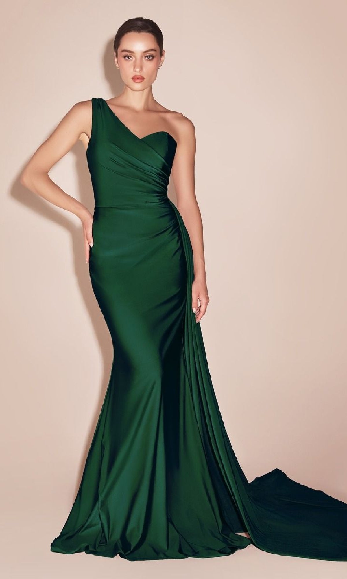 Woman modeling the Side-Sash One-Shoulder Long Prom Dress PT004 in dark green, featuring a fitted floor-length silhouette and slight train, standing against a plain beige background.