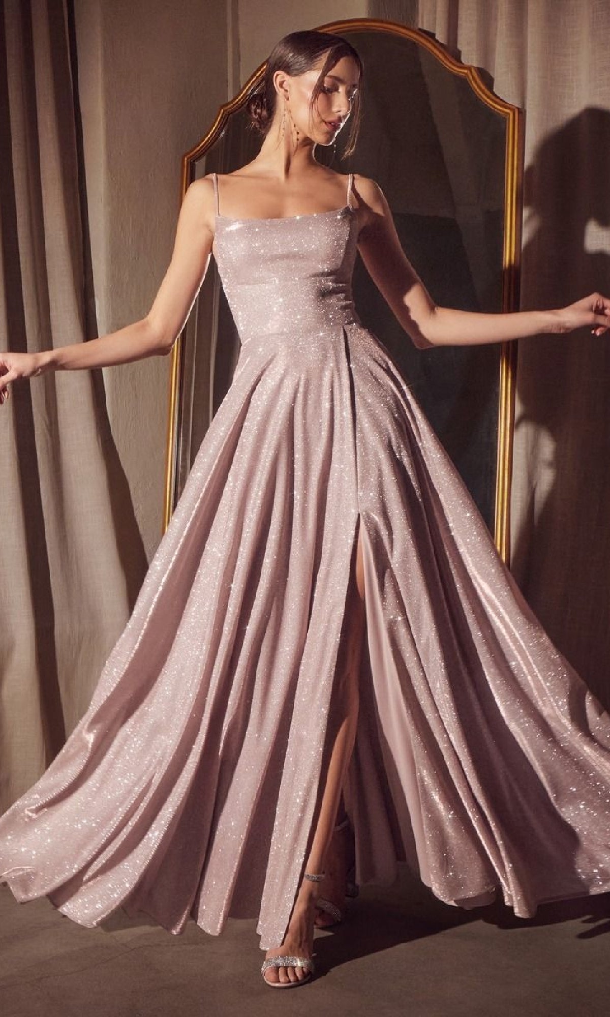 A woman poses in front of a mirror wearing the Classic Long Glitter Prom Dress: Amoris T213, a sparkling light pink A-line formal dress with thin straps and a high slit.