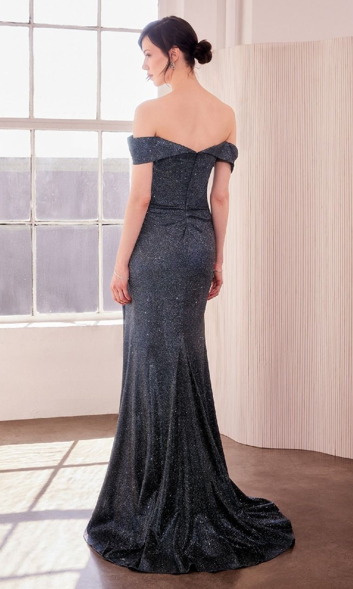 A woman stands in a well-lit room wearing the Off-the-Shoulder Glitter Prom Gown: Amoris T605, her hair elegantly styled in a low bun.