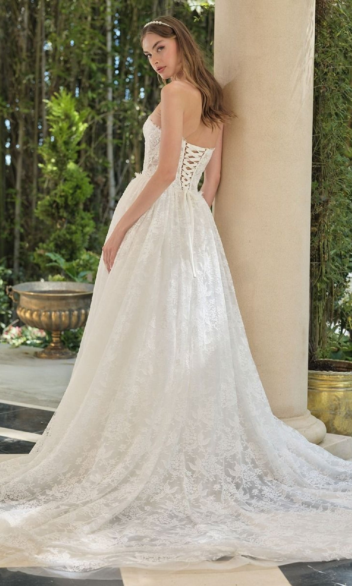 Woman in a white lace wedding dress standing outdoors near columns and greenery.