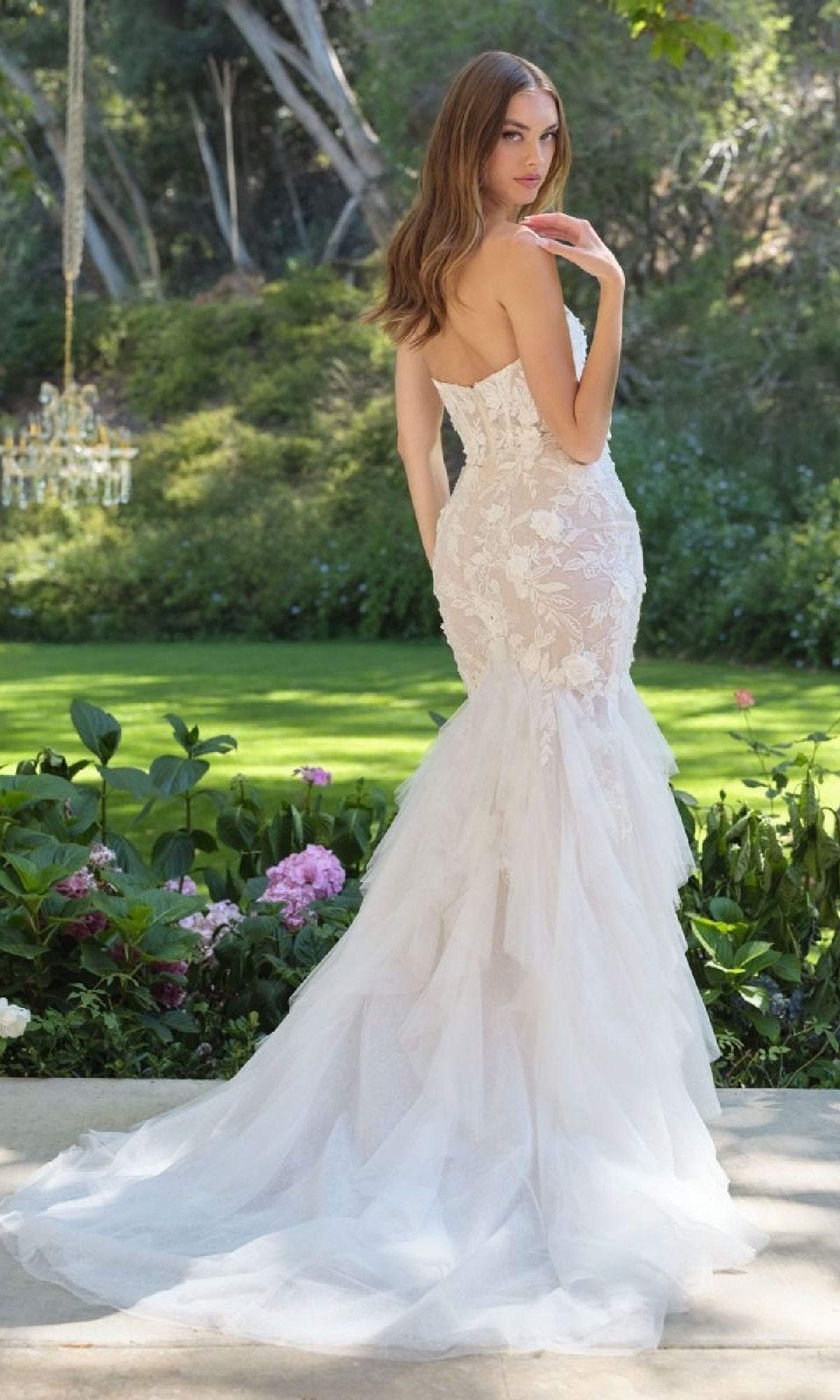 Woman showing the back of a white wedding dress she's wearing standing in a garden setting