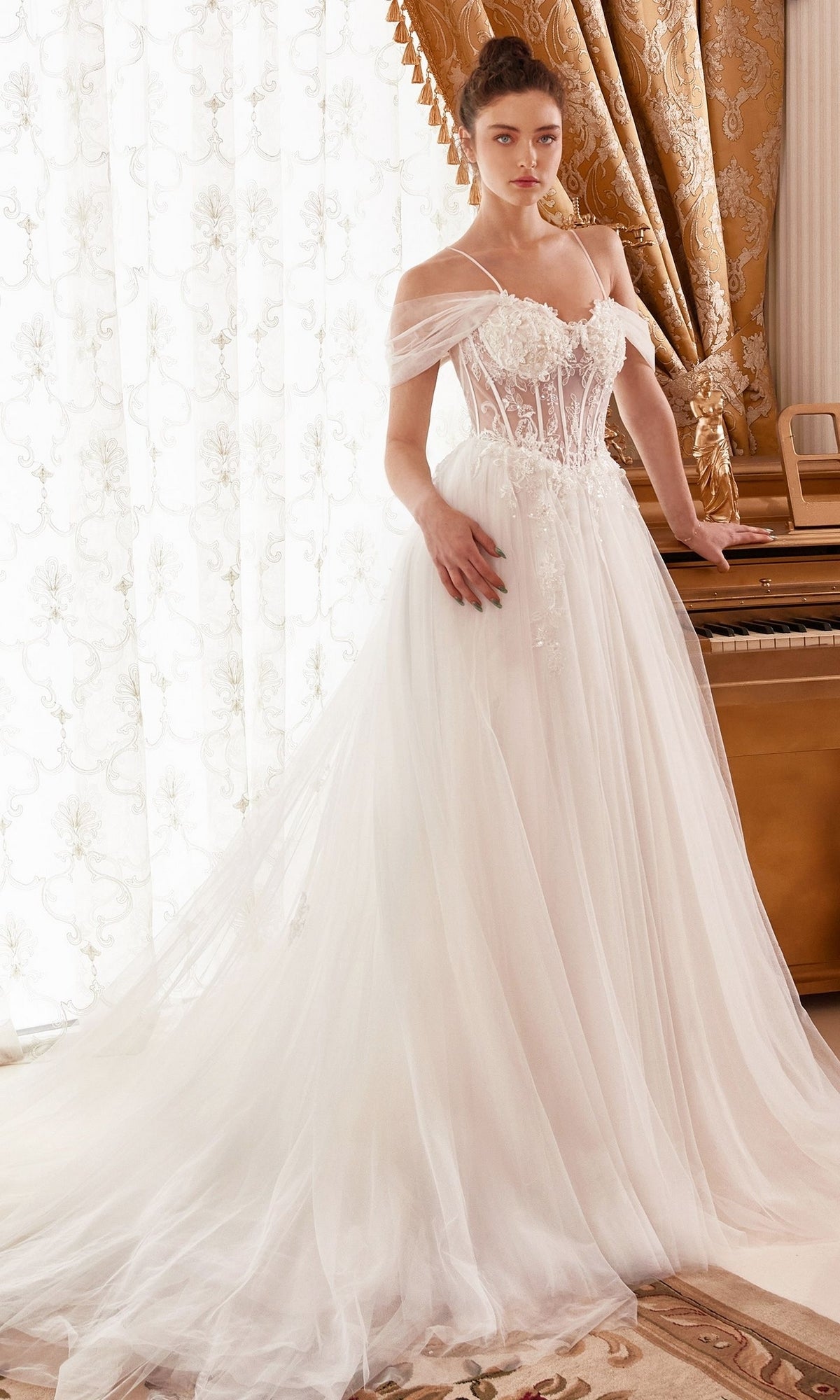 A woman in the Off-White Sheer-Bodice Long Ball Gown WN307 with floral details stands by a piano in a room adorned with gold curtains.