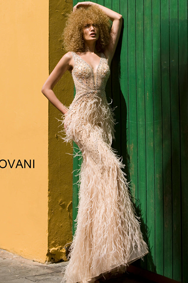 A woman with curly hair models the Jovani Sheer-Bodice Long Prom Dress with Feathers, standing by a green wooden wall next to a yellow building.