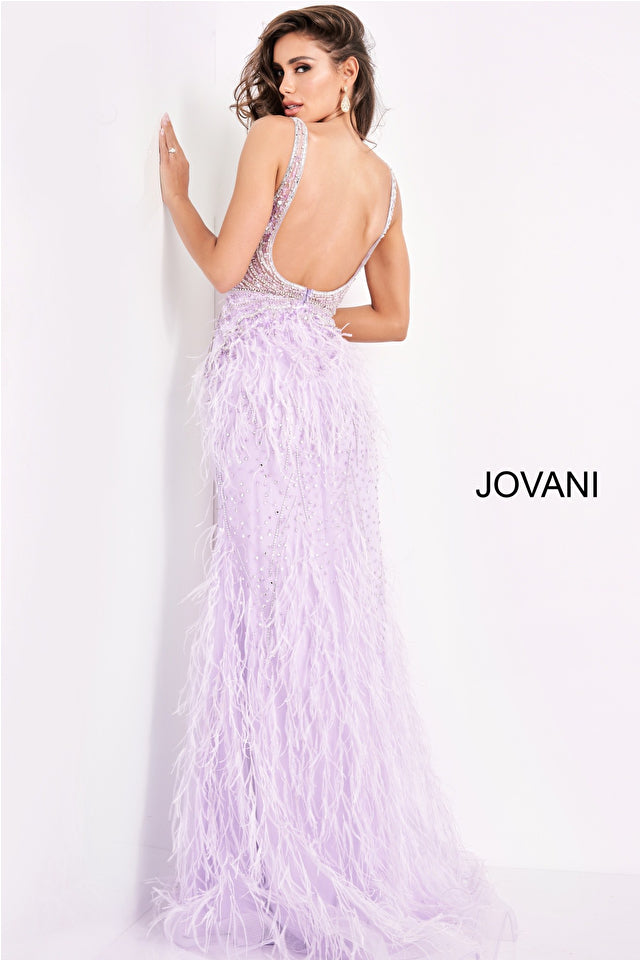 A woman in the Jovani Sheer-Bodice Long Prom Dress with Feathers, a backless light purple gown with a feathered skirt, stands against a white wall;