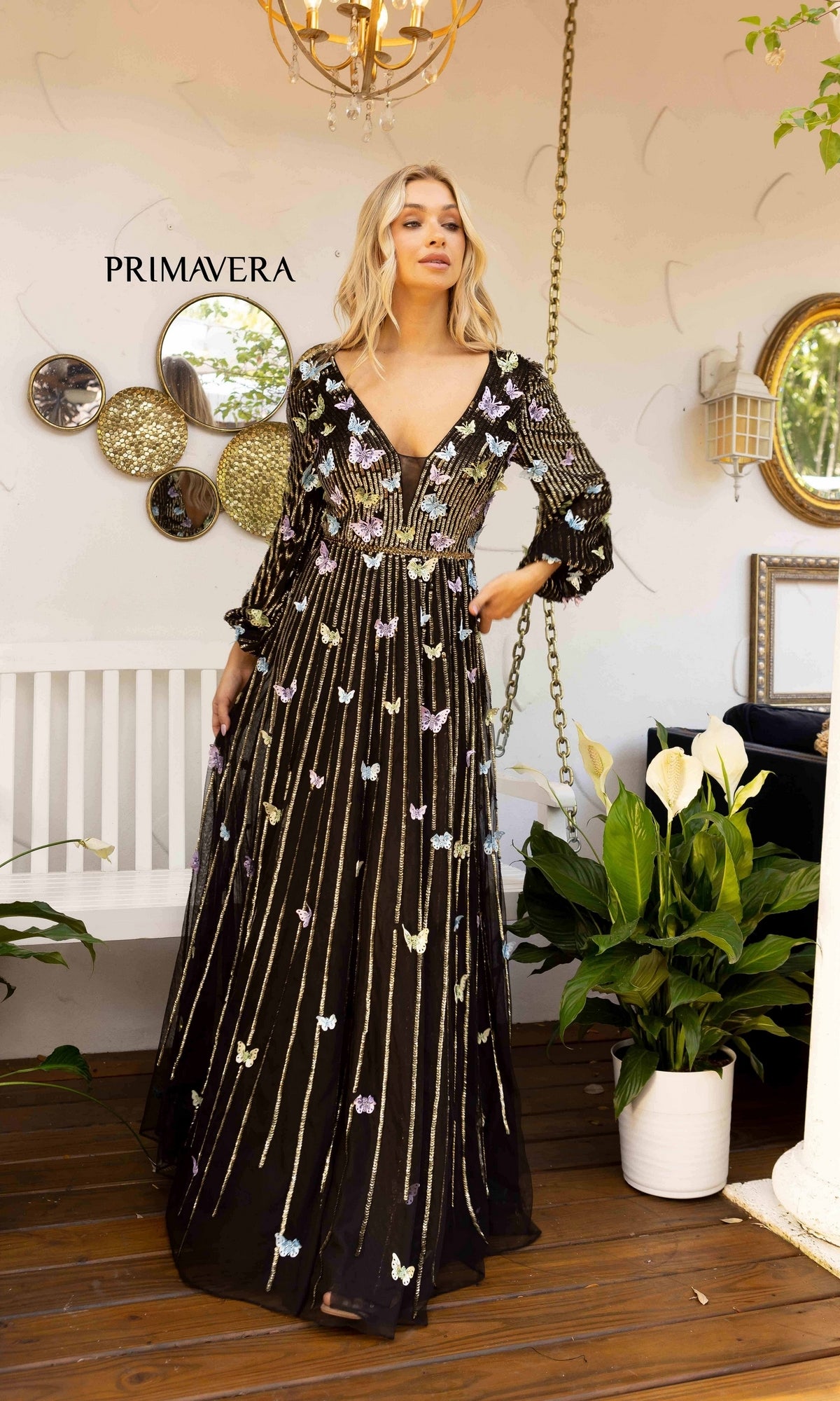 A woman stands indoors under a chandelier, wearing the Long-Sleeve Sequin-Butterfly Formal Dress 12024 with gold detailing, creating an elegant evening look.