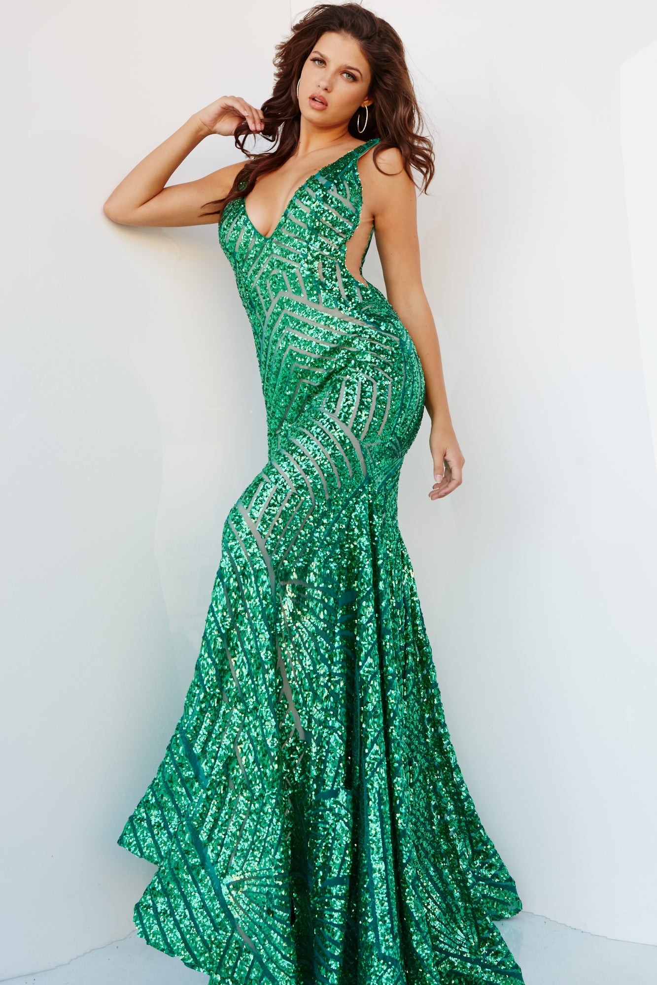 A woman poses against a plain white background wearing the Emerald Green Jovani Sequin Prom Dress 24097, a fitted, floor-length gown featuring sparkling sequins and a deep V neckline.