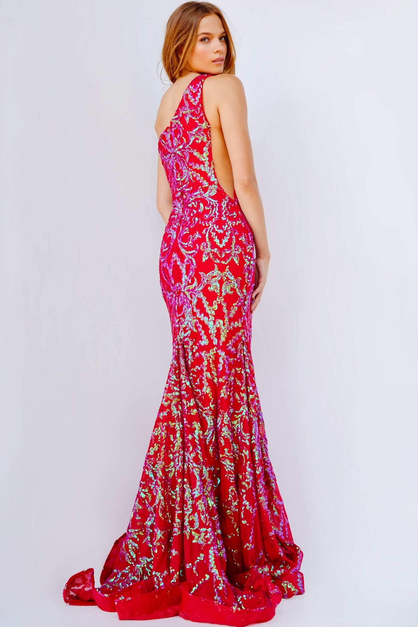 A woman poses against a plain background, looking over her shoulder in the striking One-Shoulder Jovani Red Sequin Prom Dress 22845 with an open back.