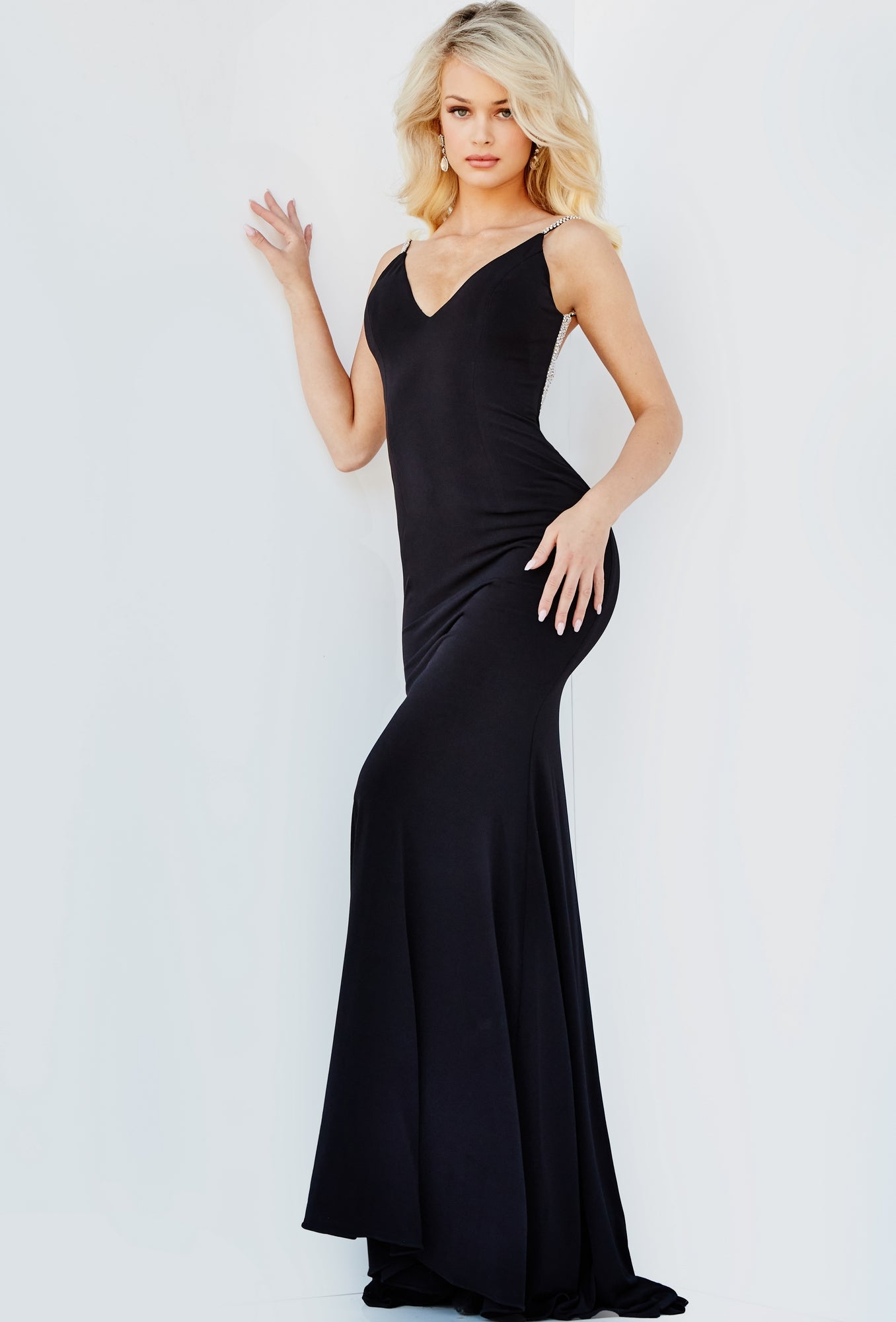 Woman wearing the Fitted Backless Long Jovani Prom Gown 07297, a form-fitting black mermaid dress with thin straps, standing against a white background.