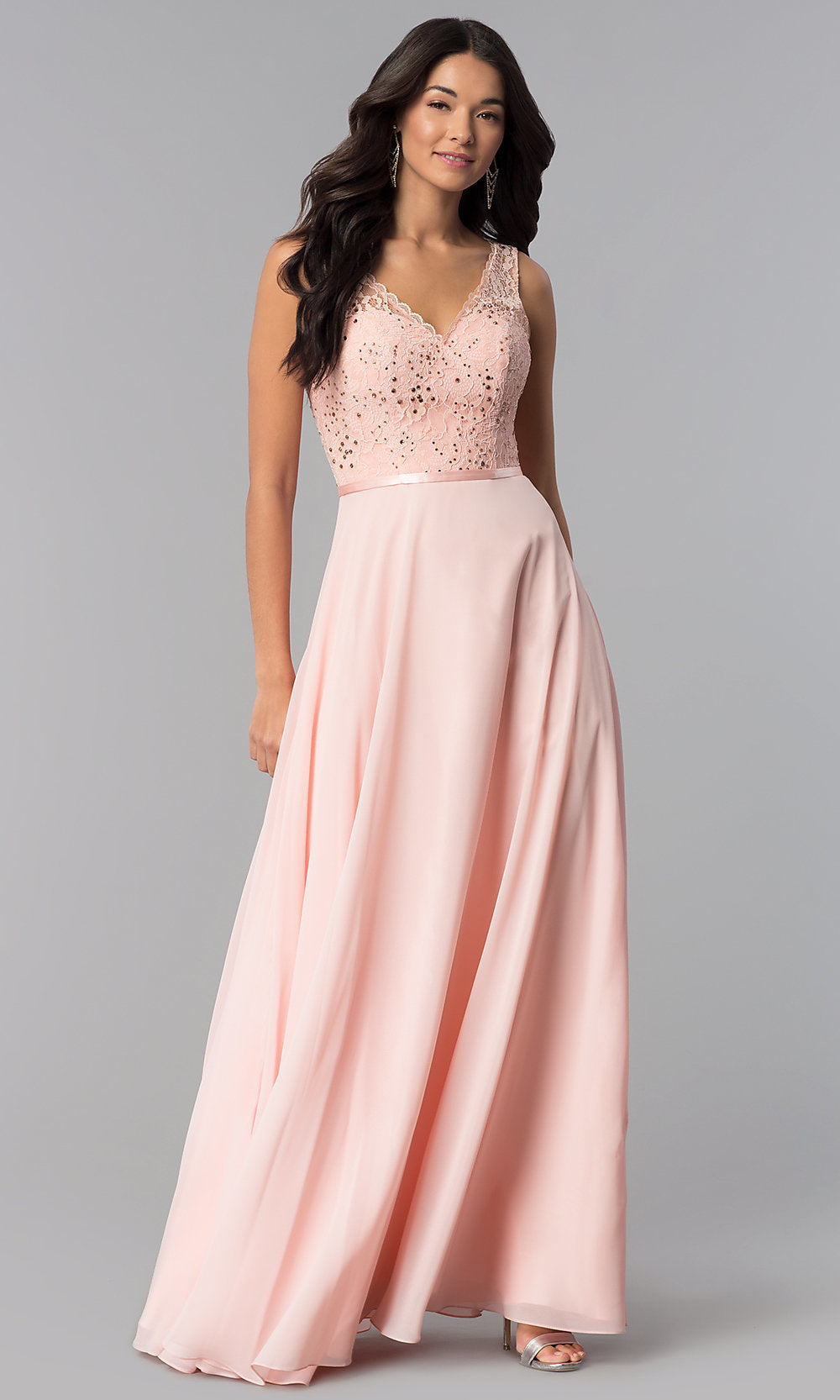 A woman stands against a plain gray background in a V-Neck Sleeveless Lace-Bodice Long Prom Dress featuring a flowing skirt and fitted bodice.