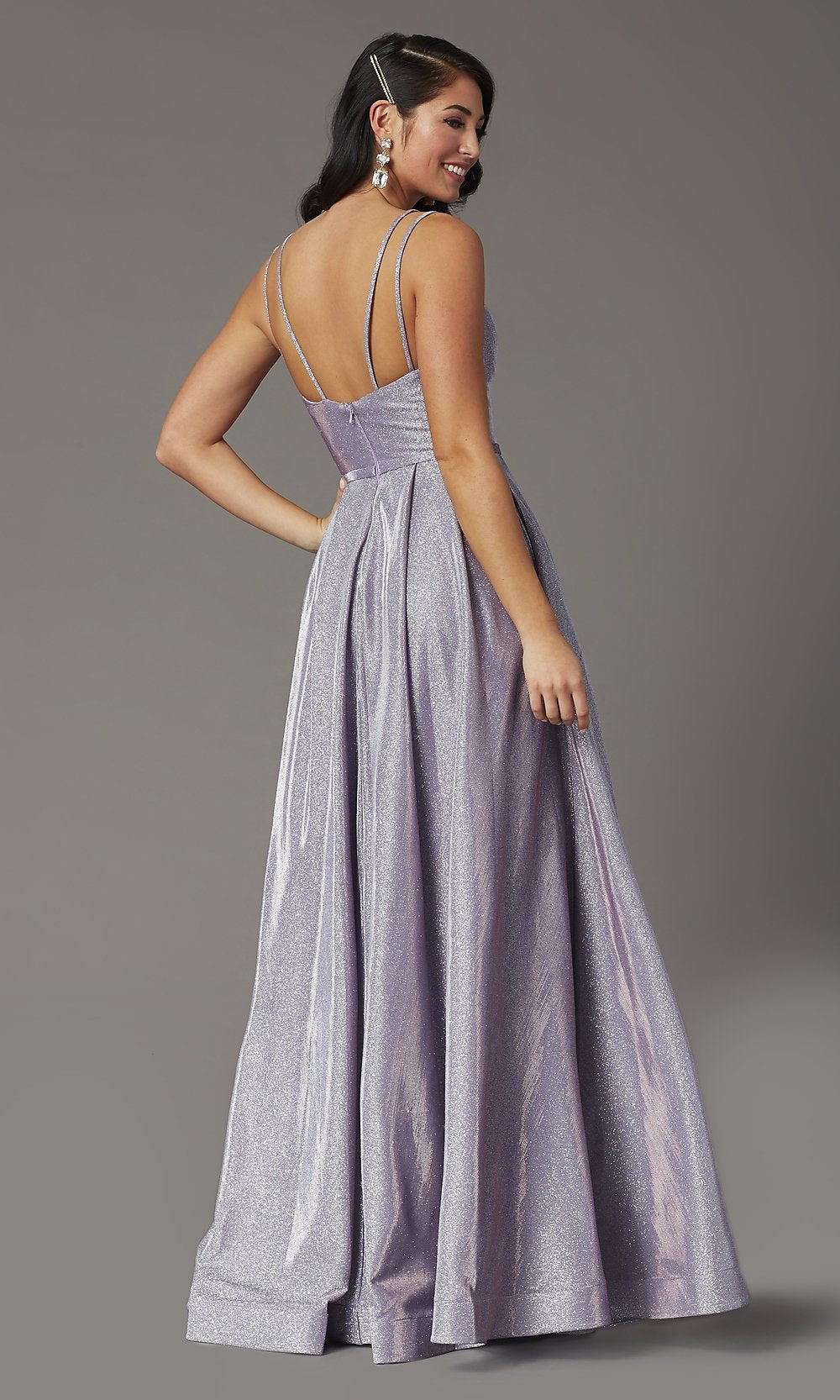 Woman models the Metallic Long A-Line Prom Dress with Side Pockets, featuring a floor-length shimmery lavender metallic jersey and thin straps, photographed from the back against a plain gray background.