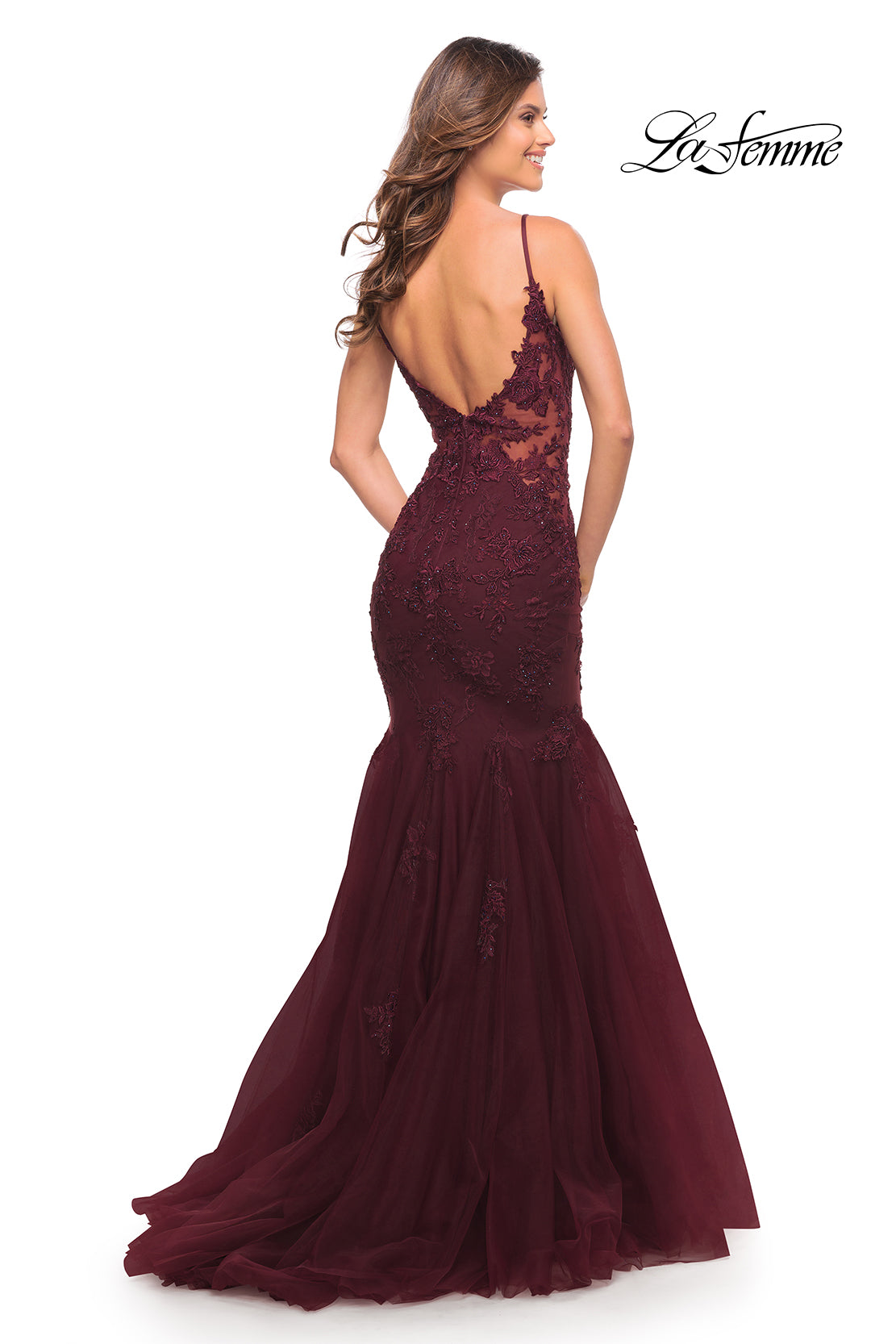 A woman stands facing away in a floor-length La Femme Embroidered-Lace Long Mermaid Prom Dress with a sheer lace bodice, low back, and thin straps; deep burgundy color. La Femme logo appears in the upper right corner.